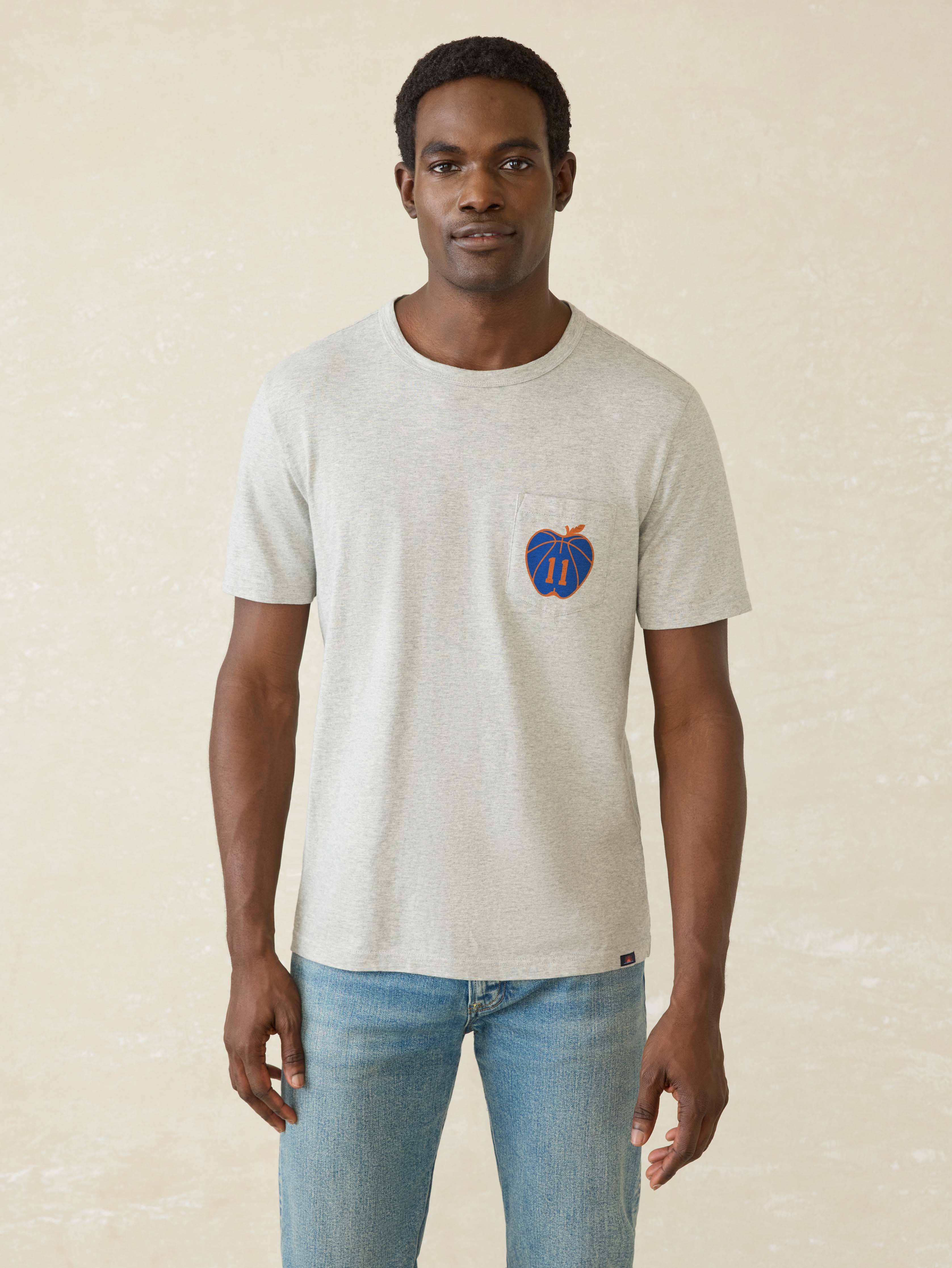 Man wearing a light gray t-shirt with a blue logo on a beige background