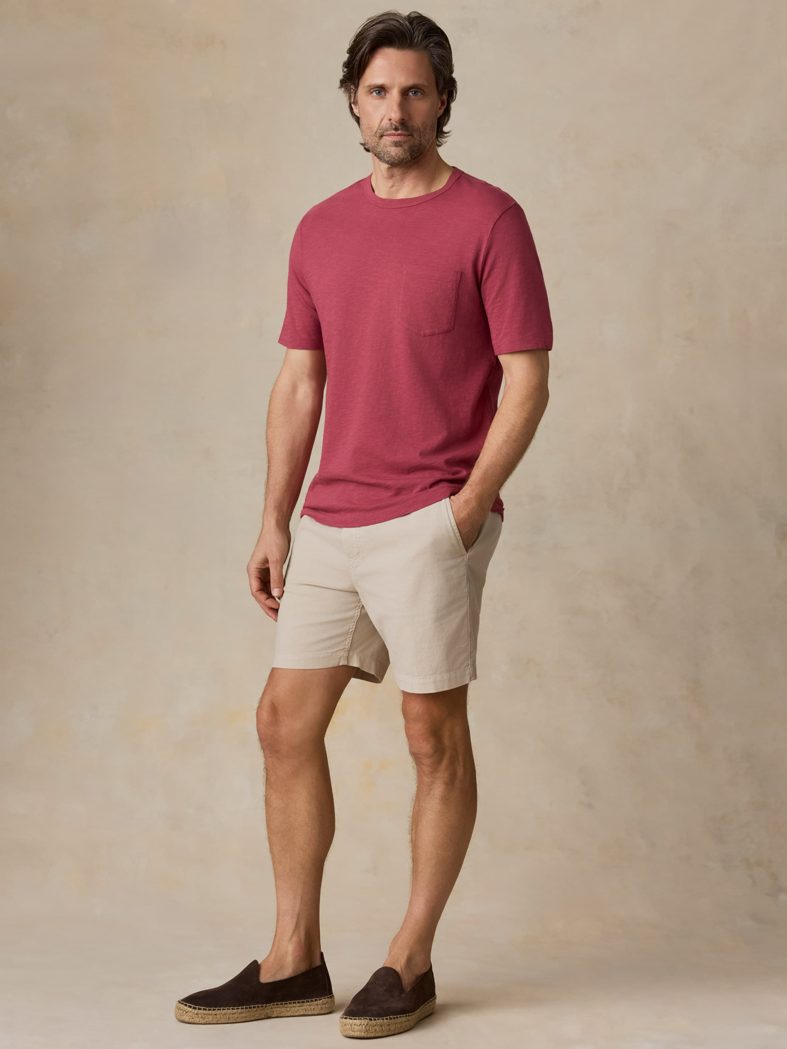 Man wearing a red t-shirt and beige shorts against a beige background