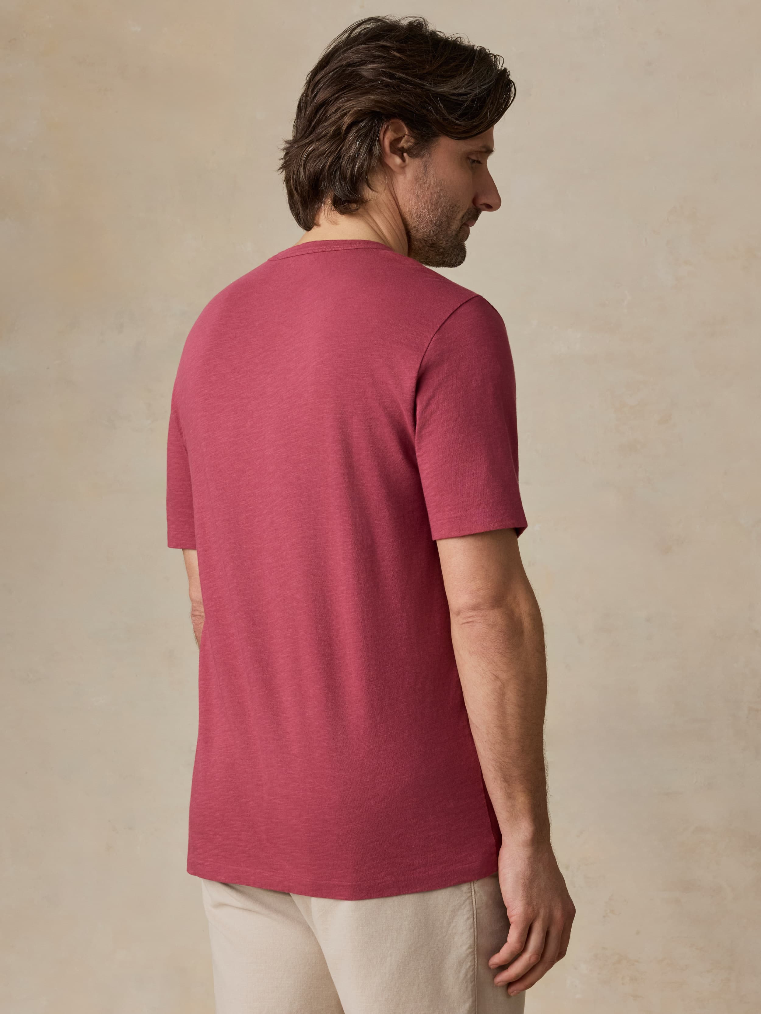 Man wearing a red t-shirt and beige shorts against a beige background