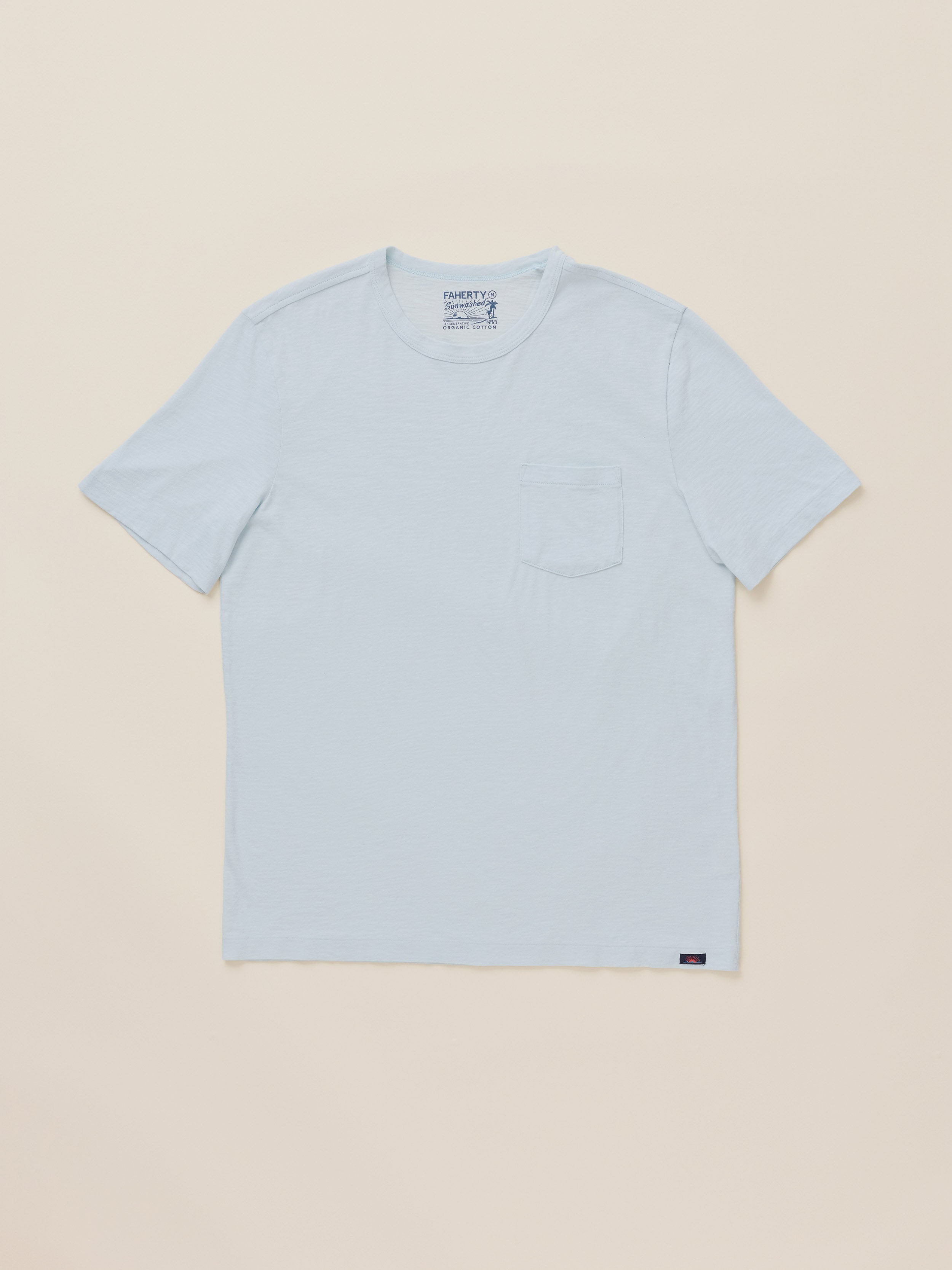 A light blue crewneck pocket t-shirt laid flat against a solid beige background.