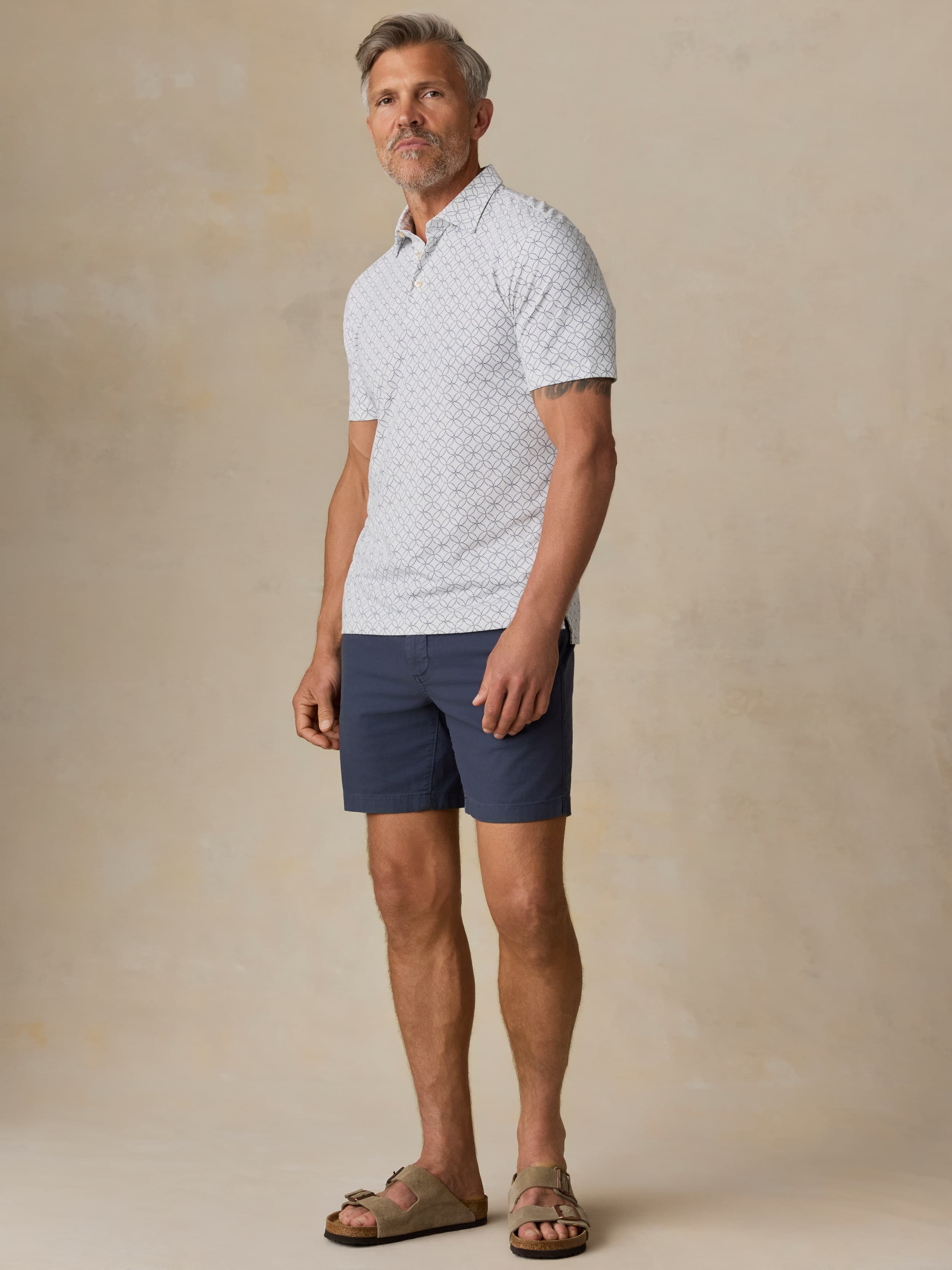 Man wearing a printed polo and navy shorts against a beige background