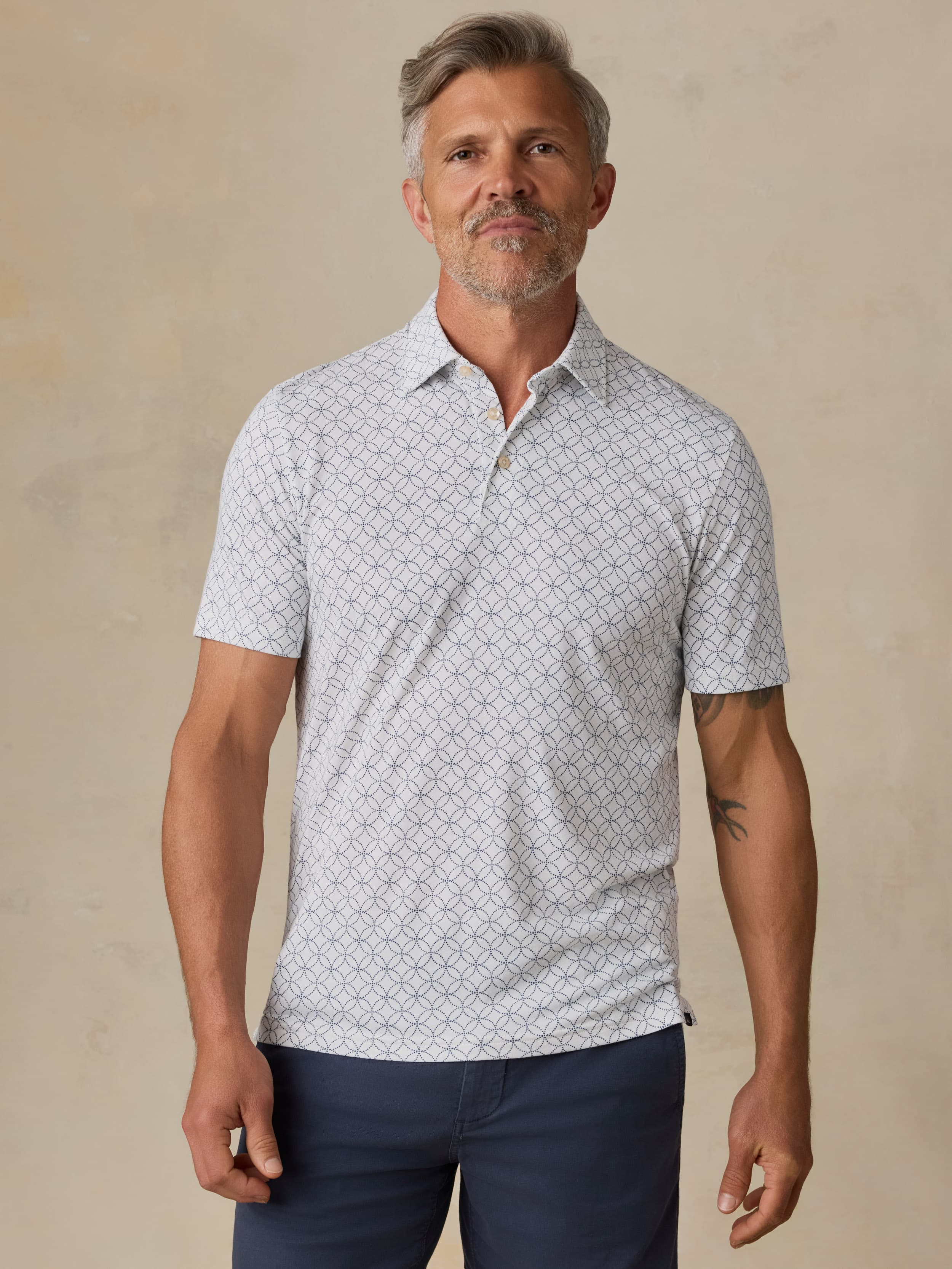 Man wearing a printed polo and navy shorts against a beige background