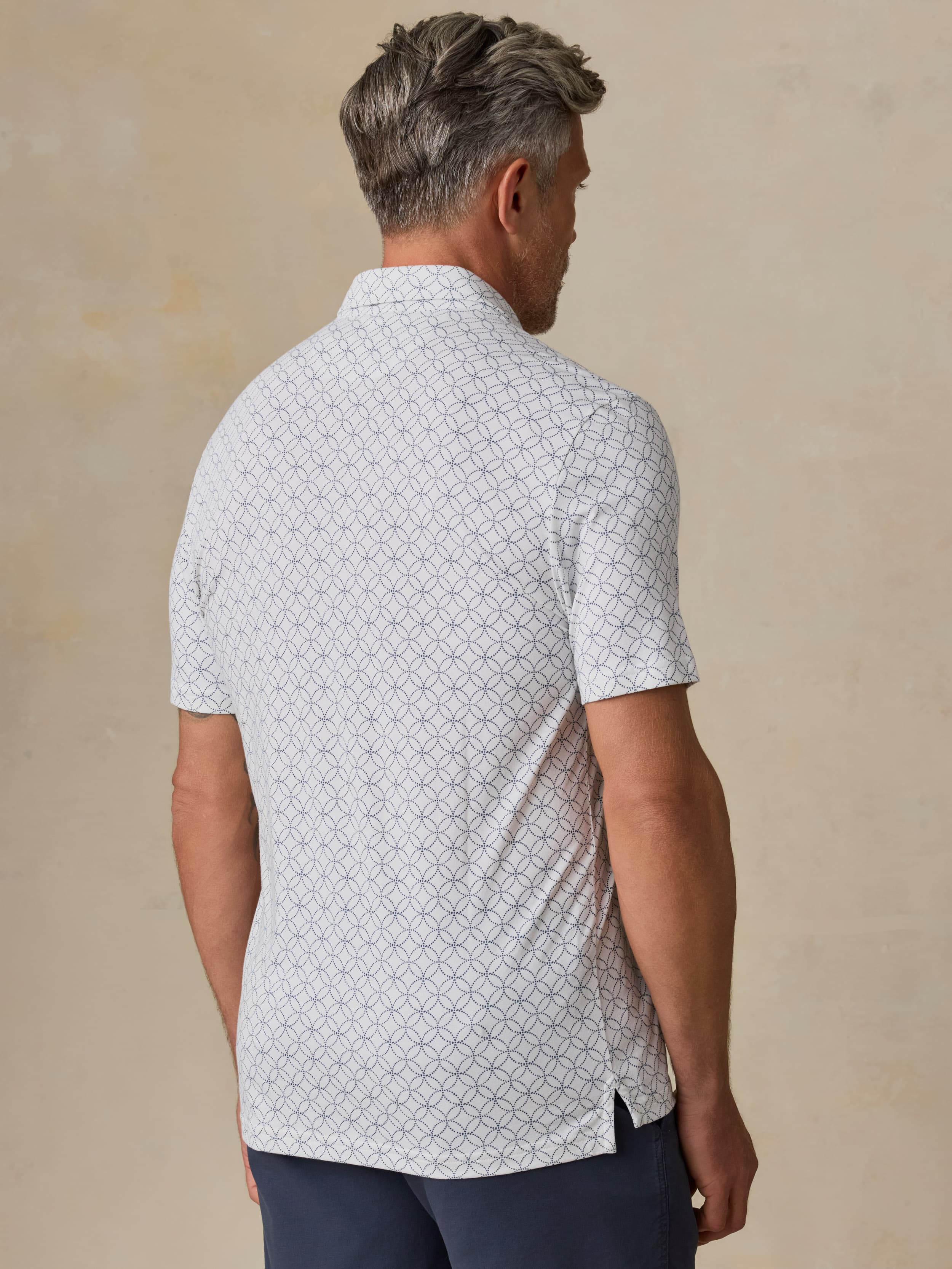 Man wearing a printed polo and navy shorts against a beige background