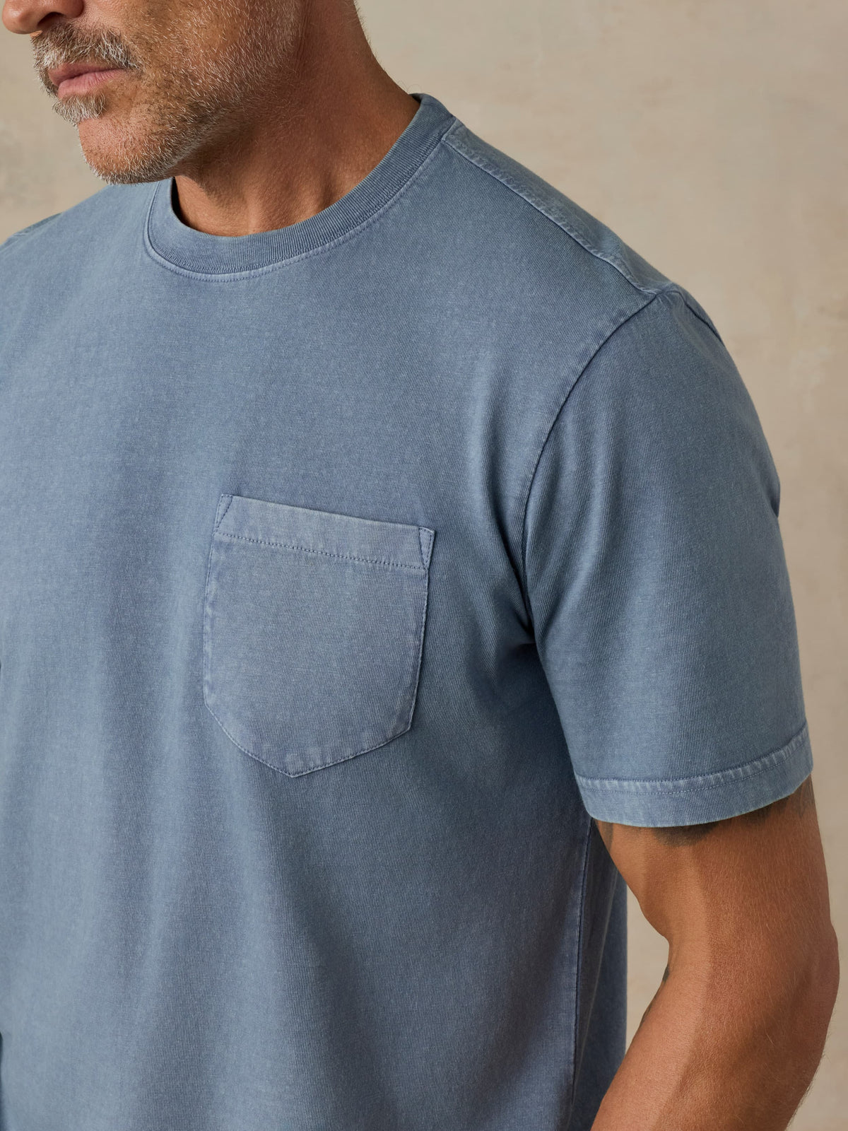 Man wearing a blue pocket tee against a beige background, image 3 of 5