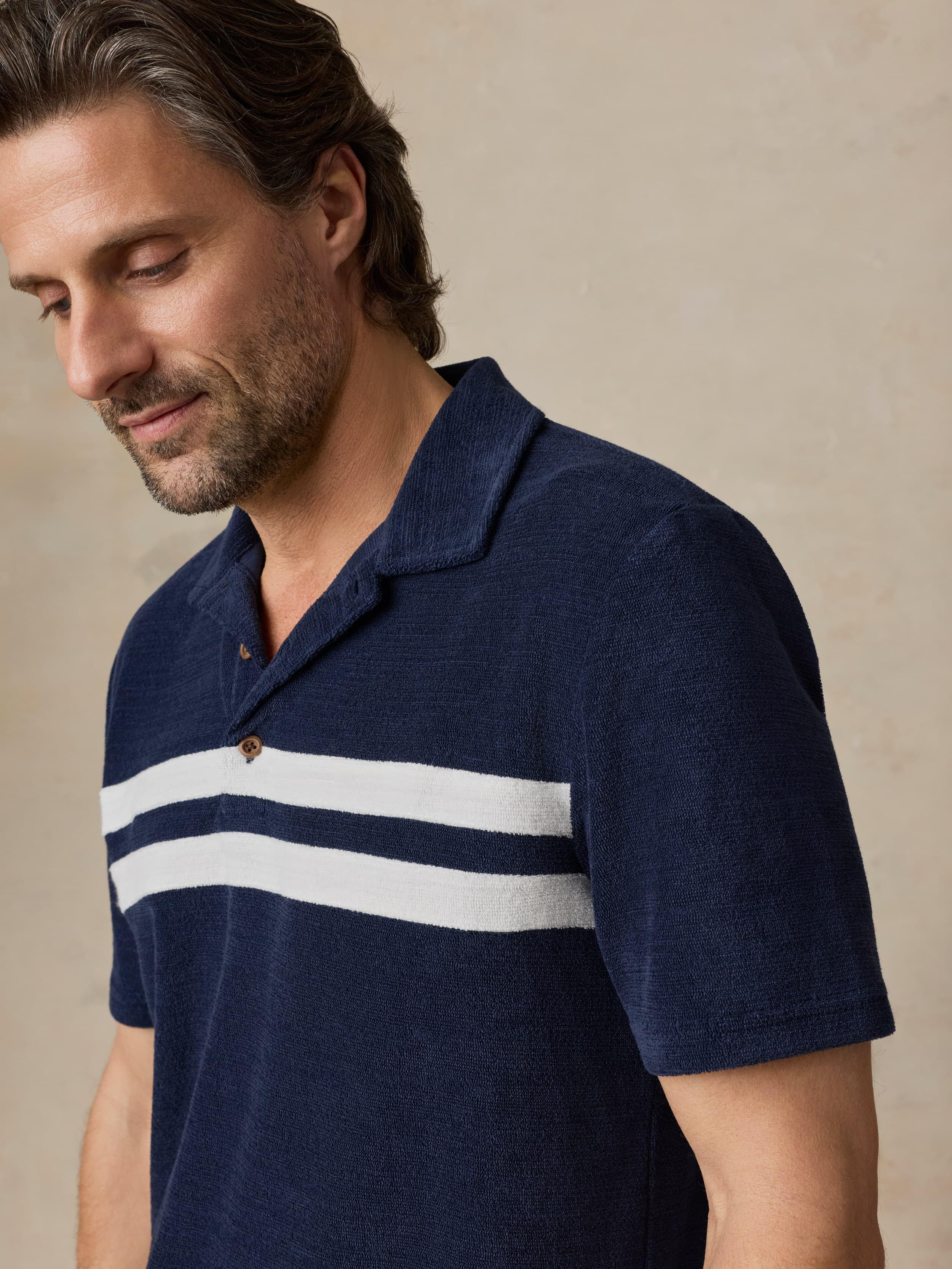 Man wearing a navy polo shirt with white stripes on a beige background