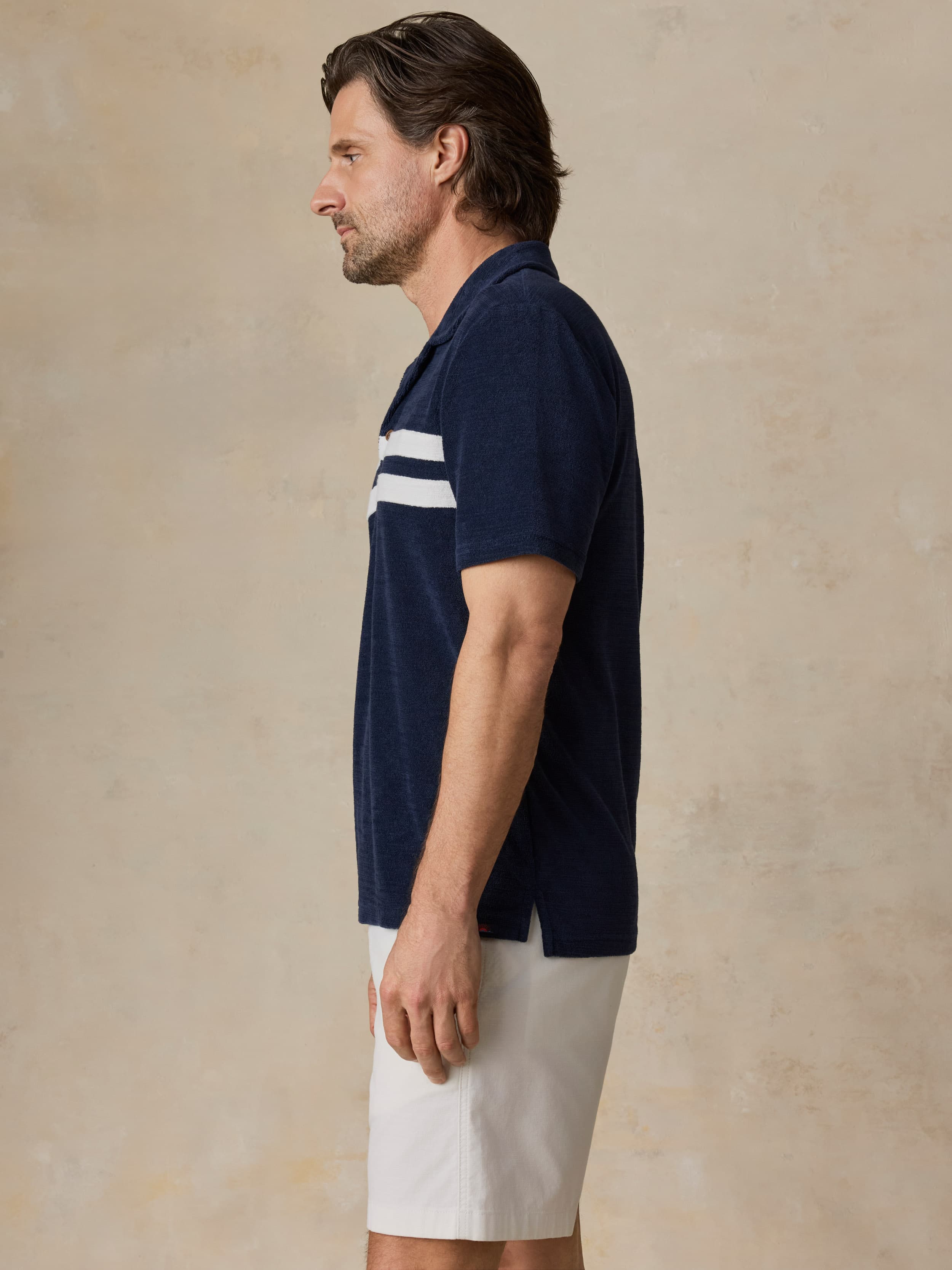 Man wearing a navy blue polo shirt with white stripes on a beige background