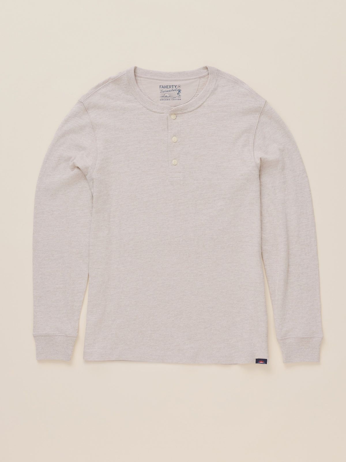 A light oatmeal heather long-sleeve henley shirt with three buttons on the collar, laid flat against a warm cream background., image 7 of 8