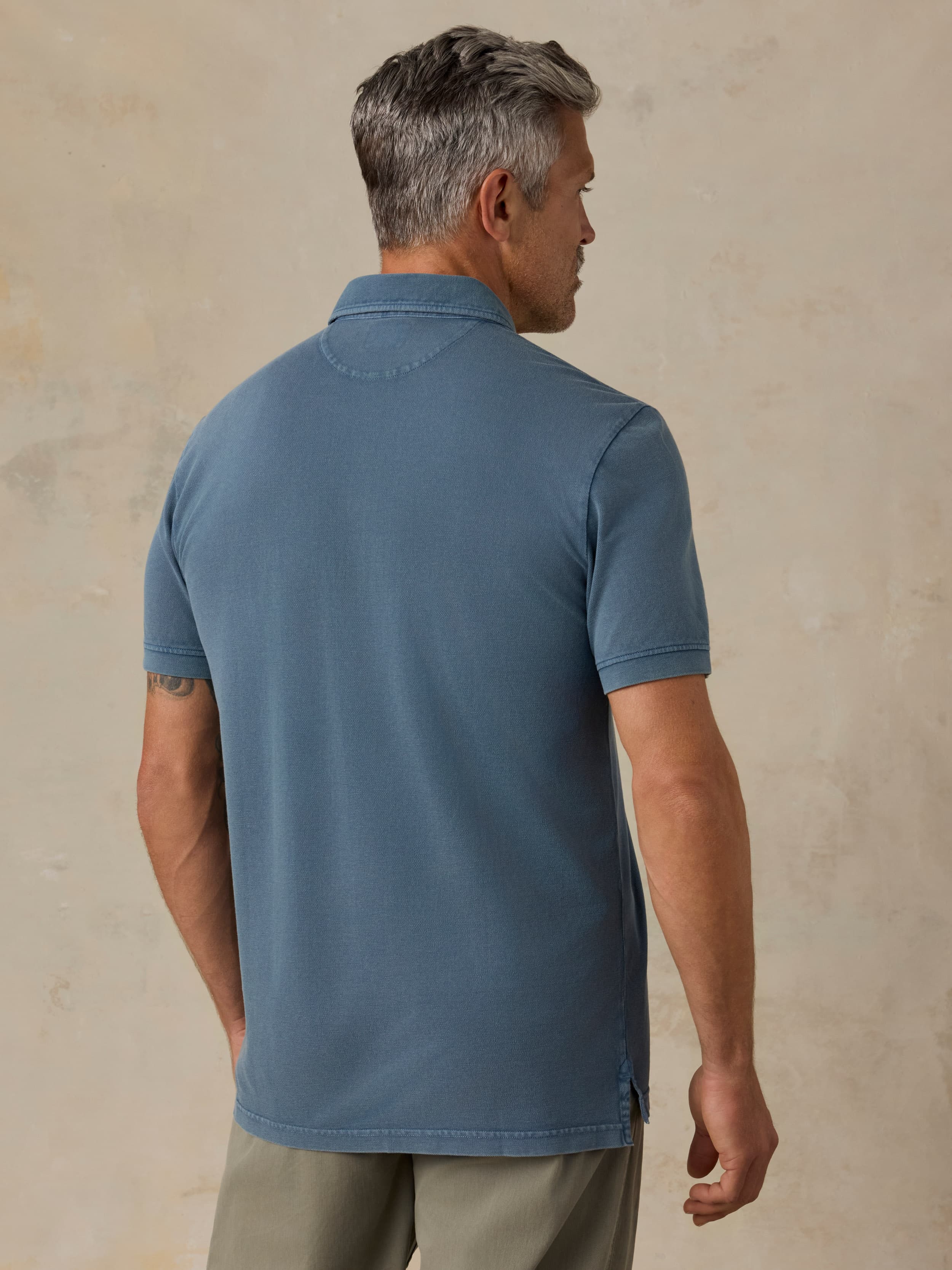 Man wearing a blue polo shirt and green pants against a beige background