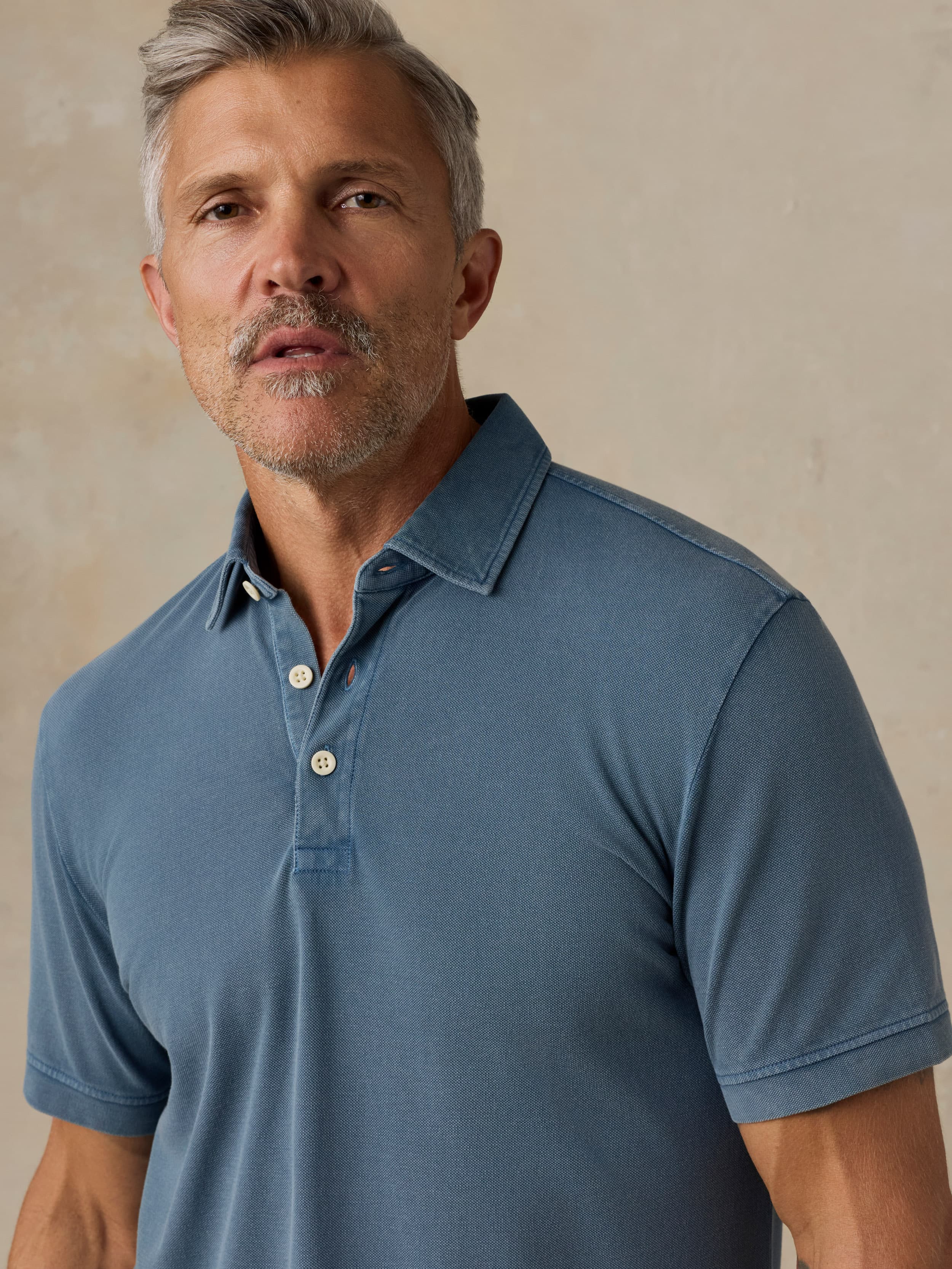 Man wearing a blue polo shirt against a beige background