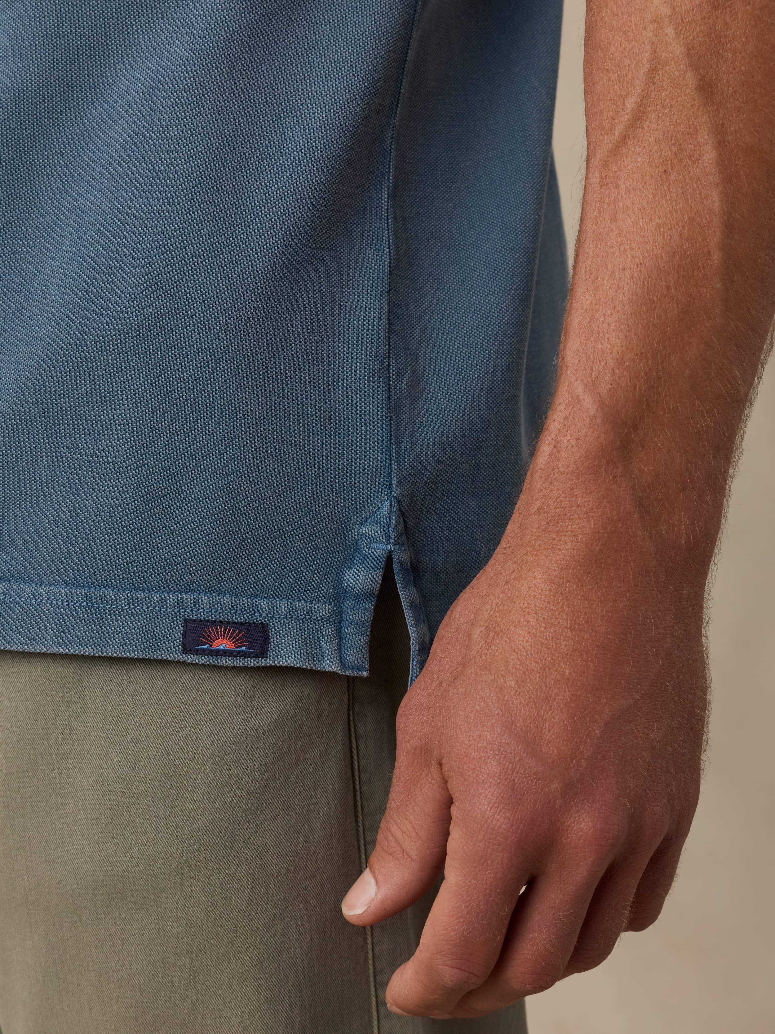 Close-up of a man wearing a blue polo shirt with a Faherty brand logo and green pants on a neutral background