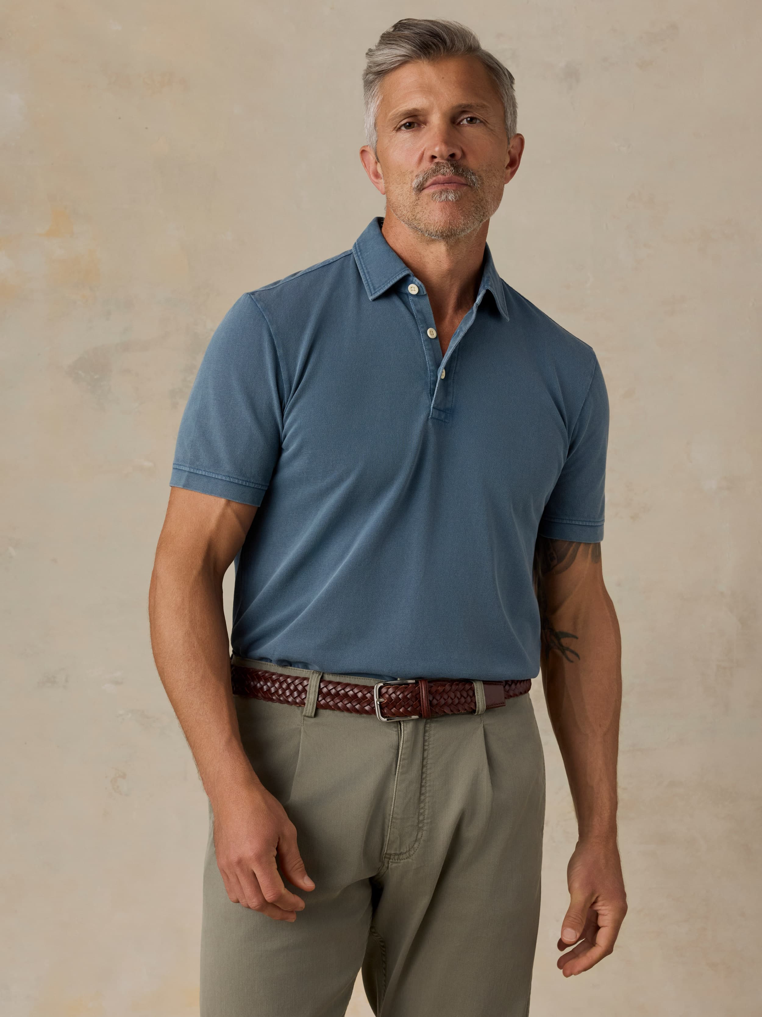 Man wearing a blue polo shirt and green pants against a beige background