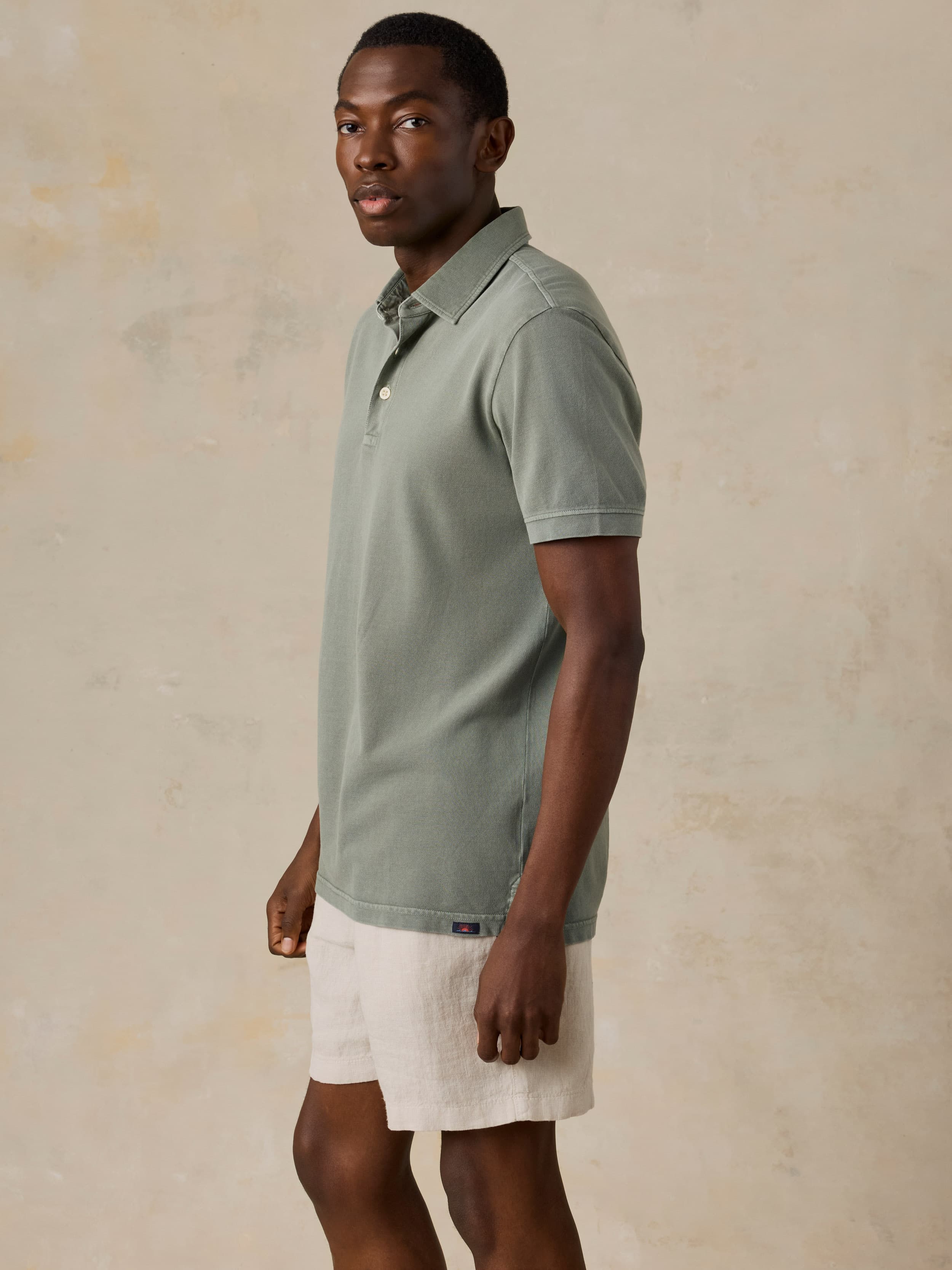 Man wearing a light green polo shirt and beige shorts against a beige background