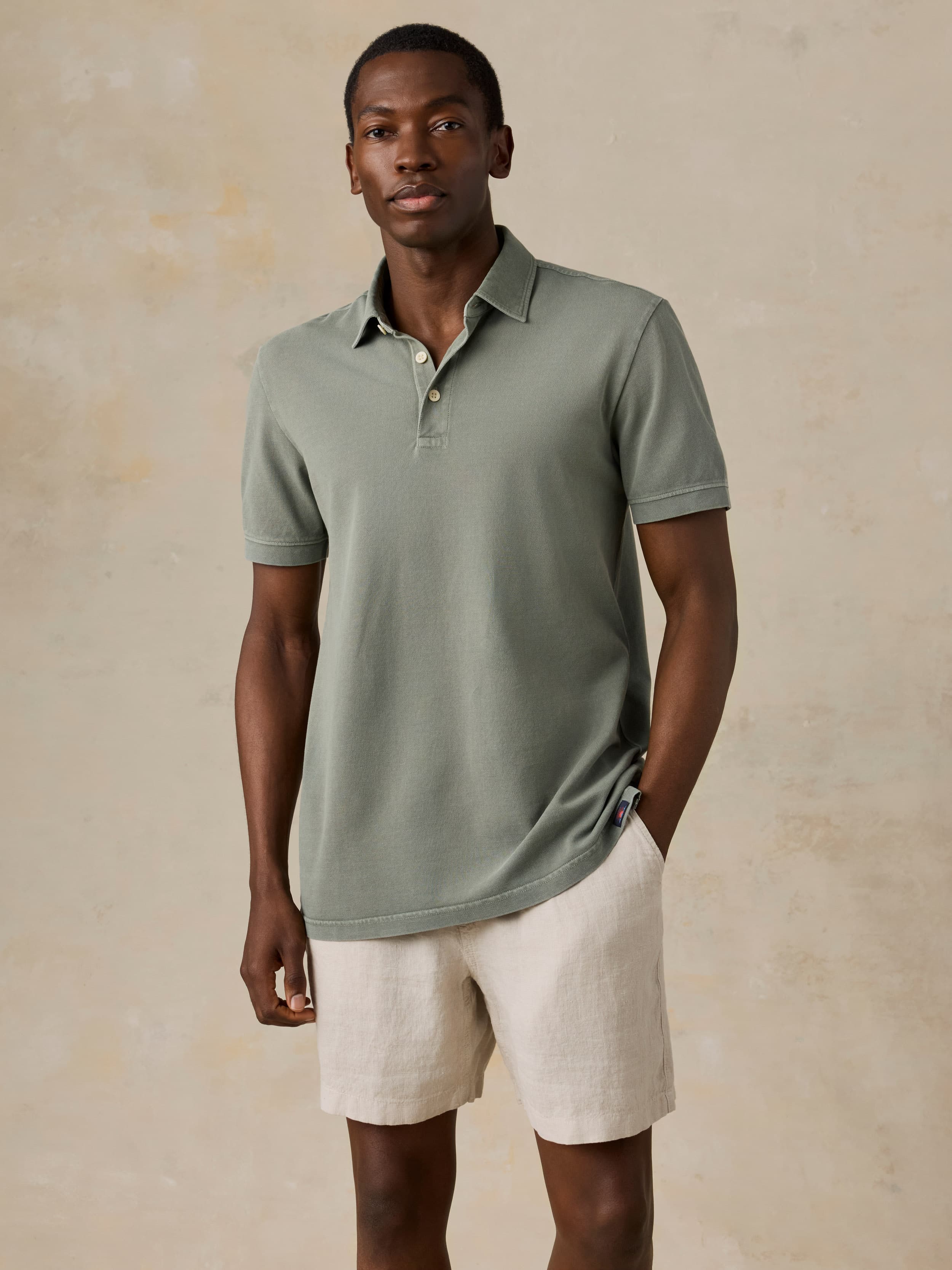 Man wearing a light green polo shirt and beige shorts against a beige background