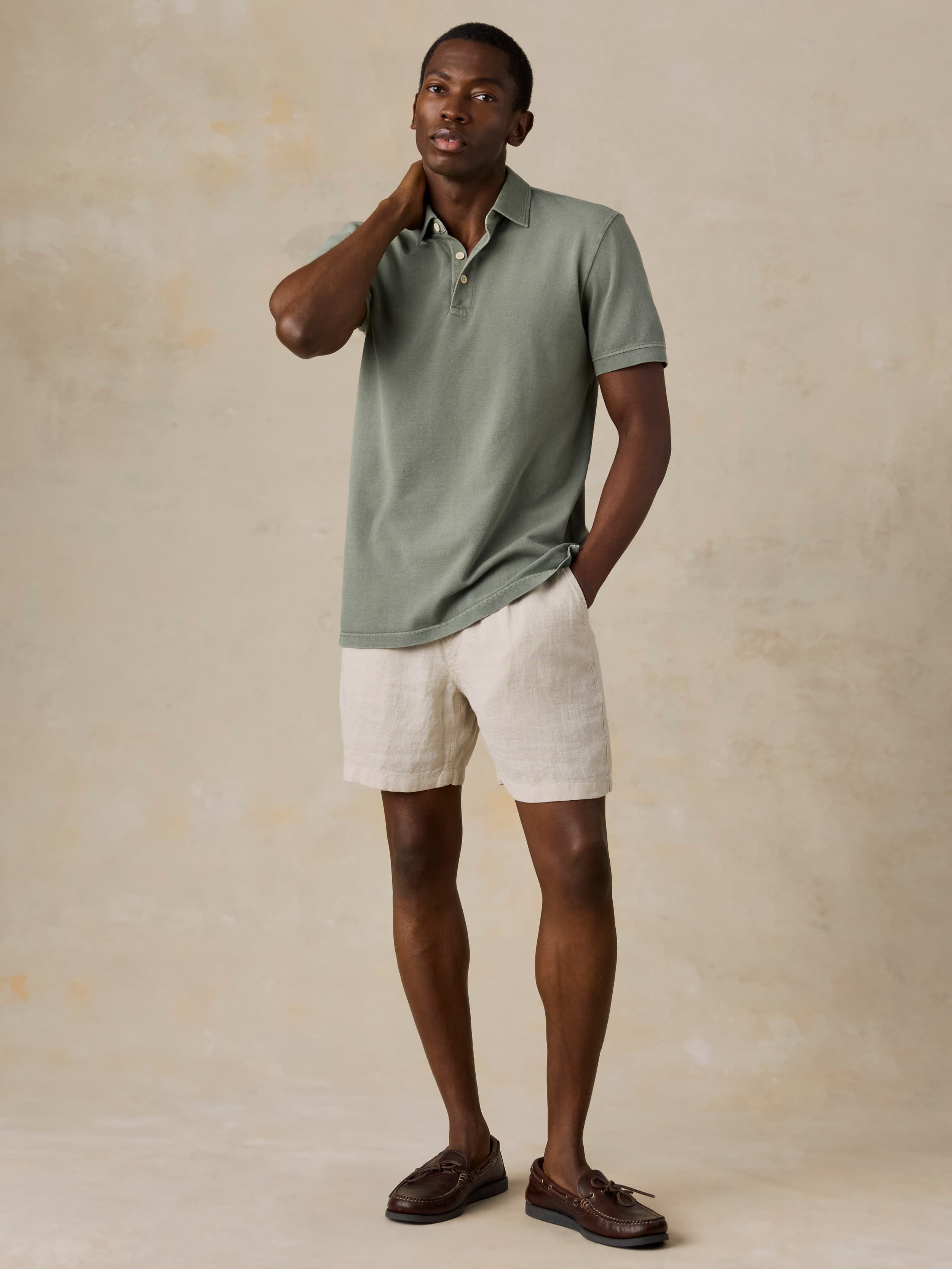 Man wearing a light green polo shirt and beige shorts against a beige background