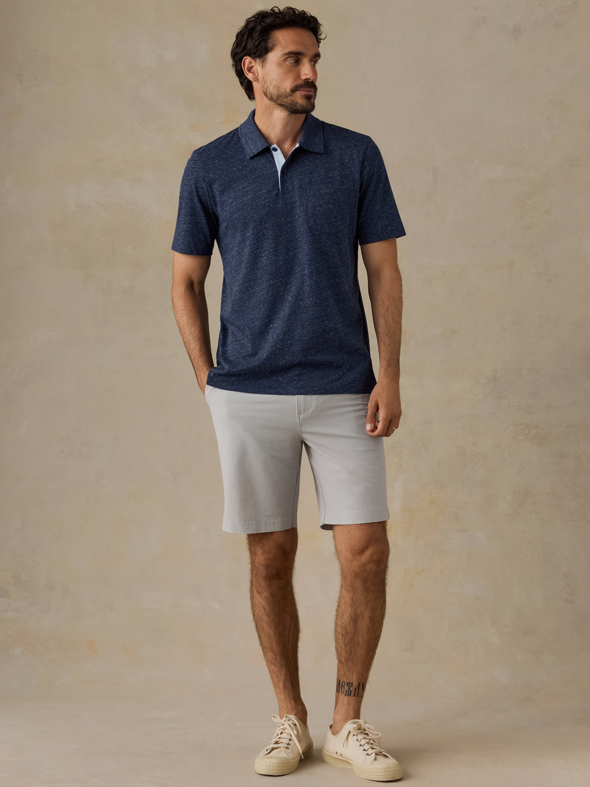 Man wearing a navy polo shirt and beige shorts against a beige background