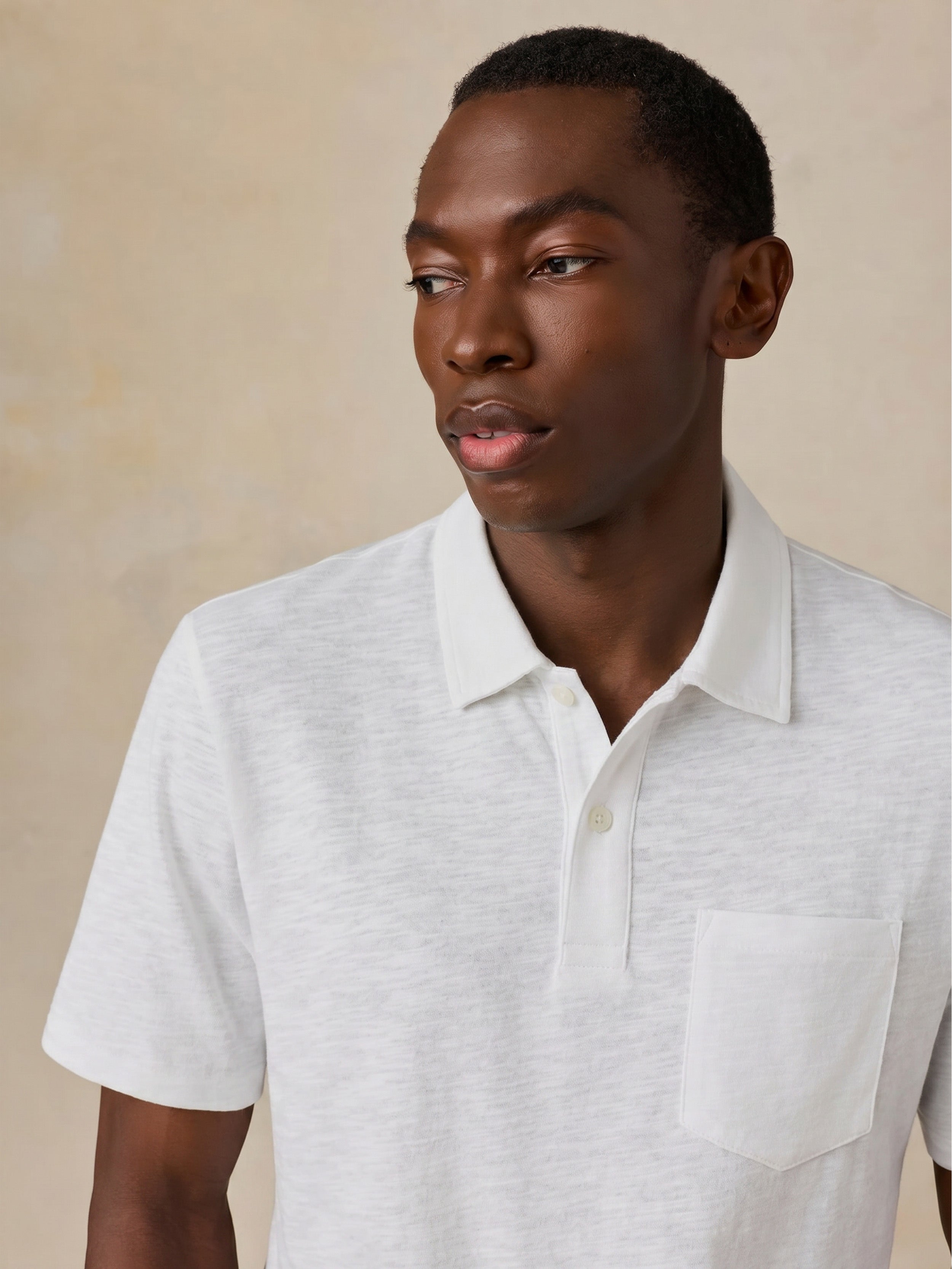 Man wearing a white short sleeve polo against a beige background