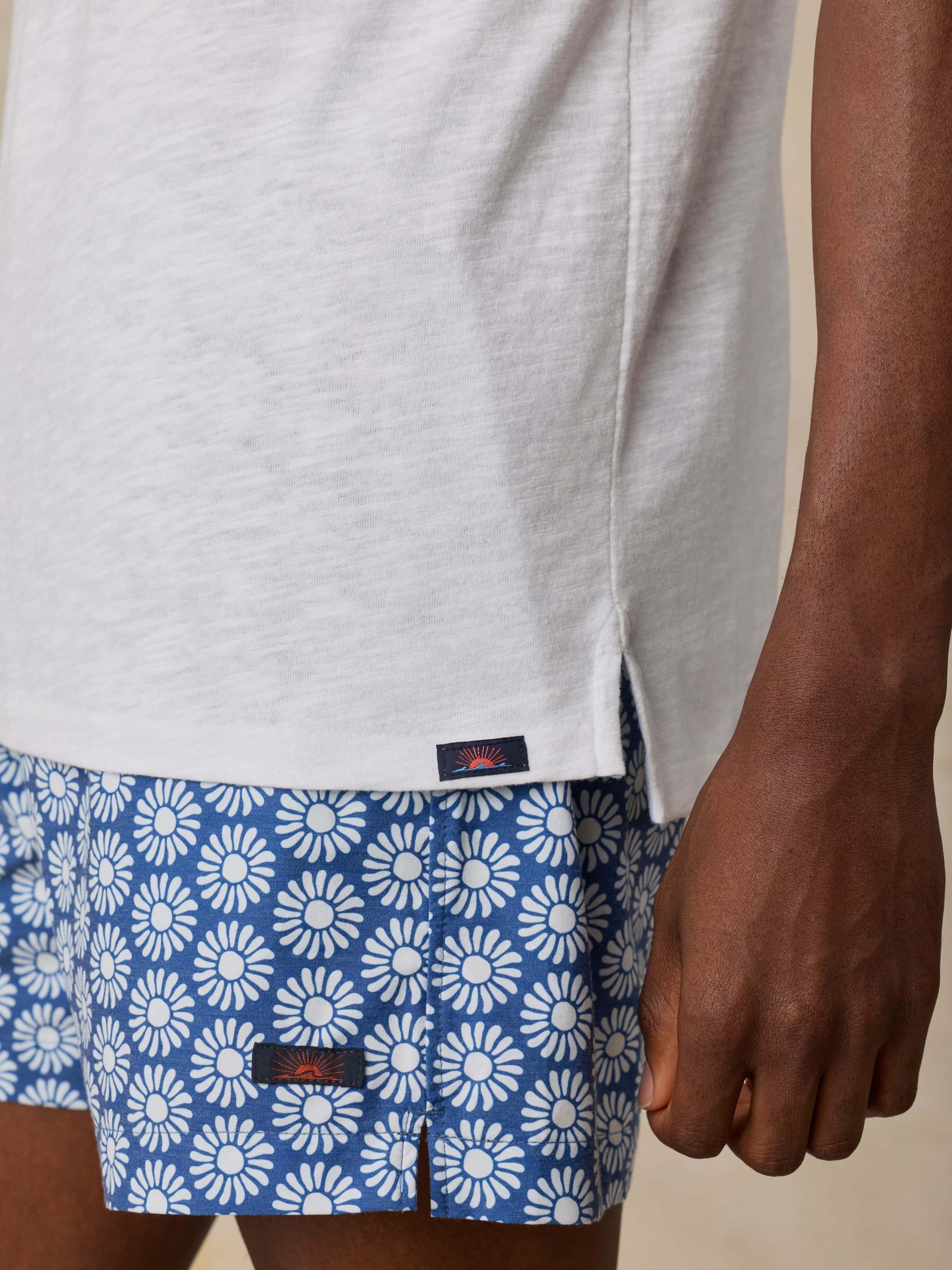 Man wearing a white short sleeve polo and blue printed swim shorts against a beige background