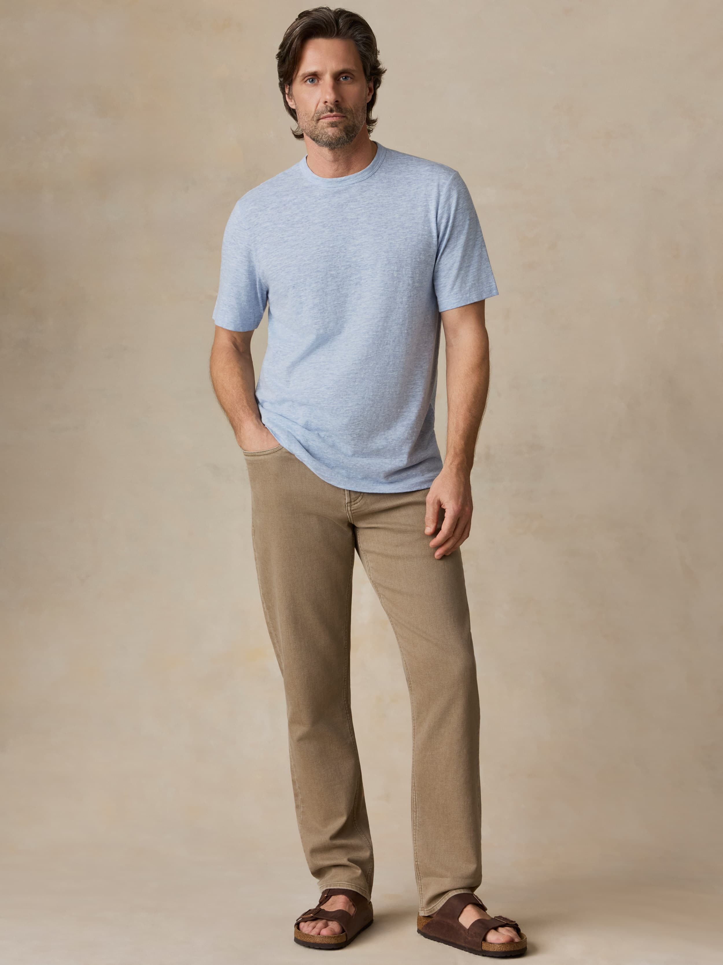 Man wearing a light blue t-shirt and beige pants against a beige background