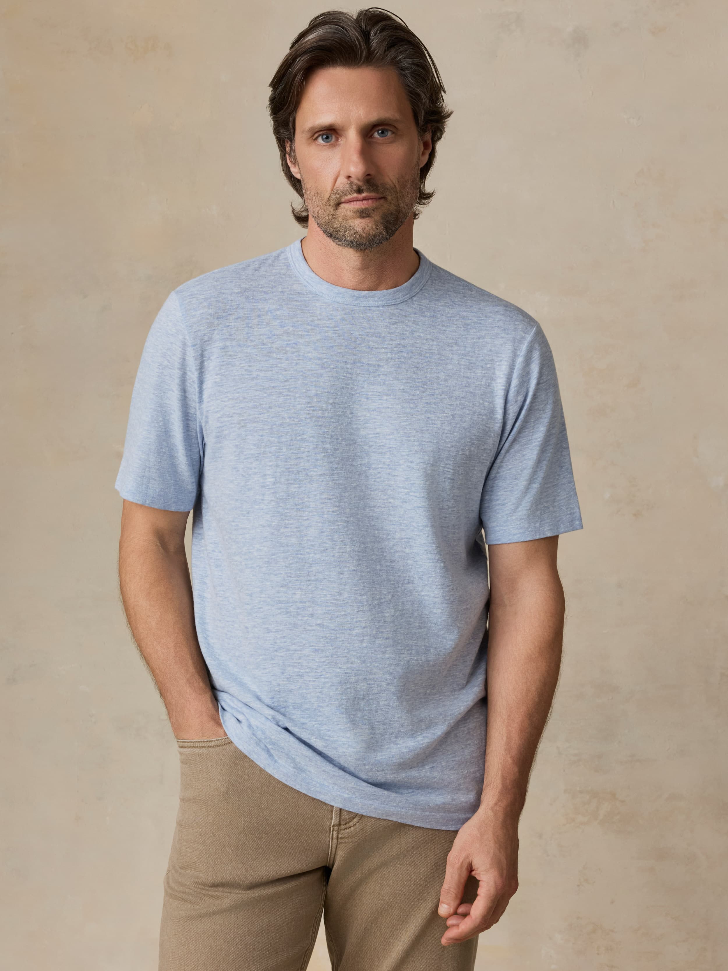 Man wearing a light blue t-shirt and beige pants against a beige background