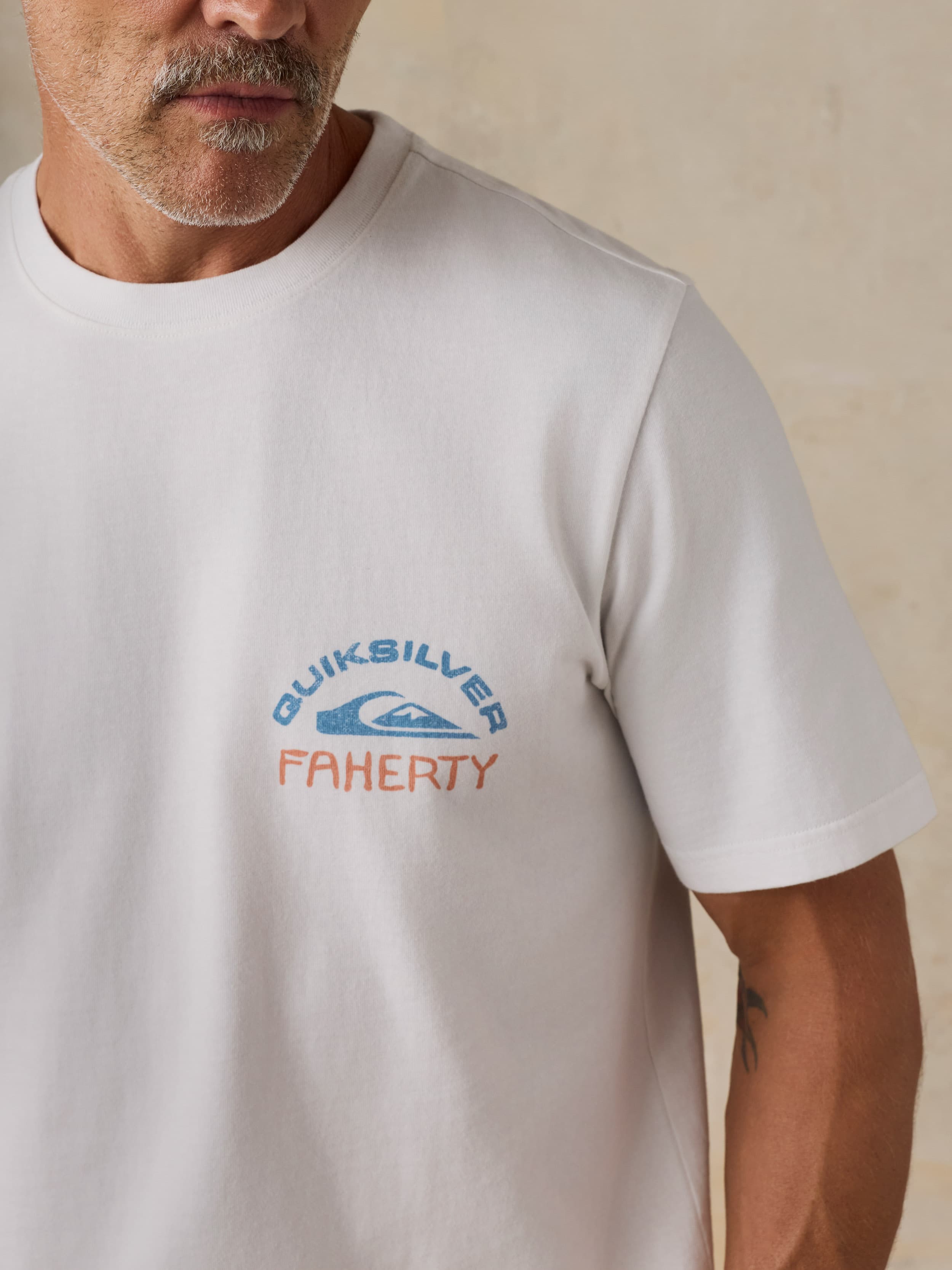 Man wearing a white Faherty x Quiksilver t-shirt against a beige background