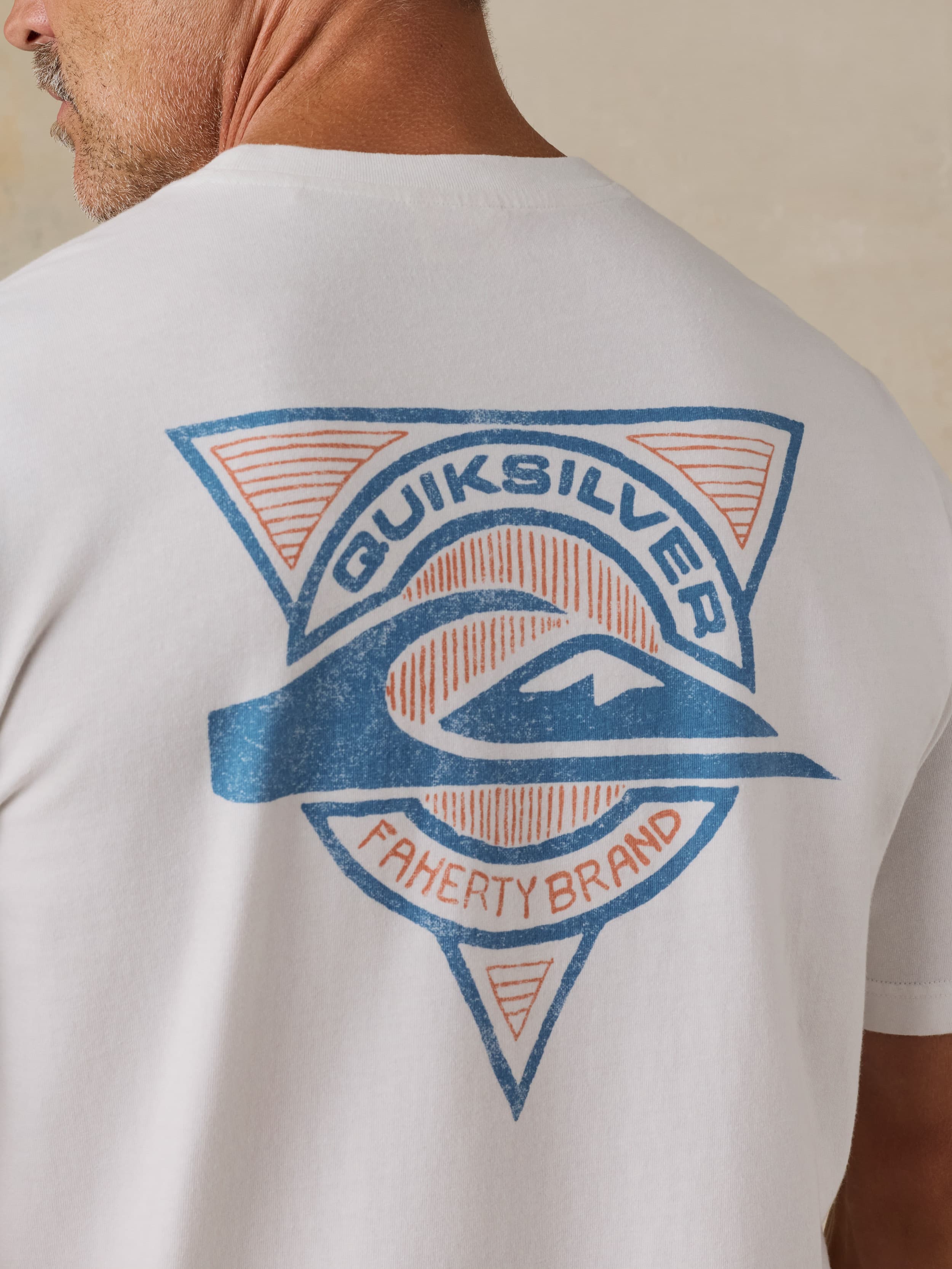 Man wearing a white Faherty x Quiksilver t-shirt against a beige background