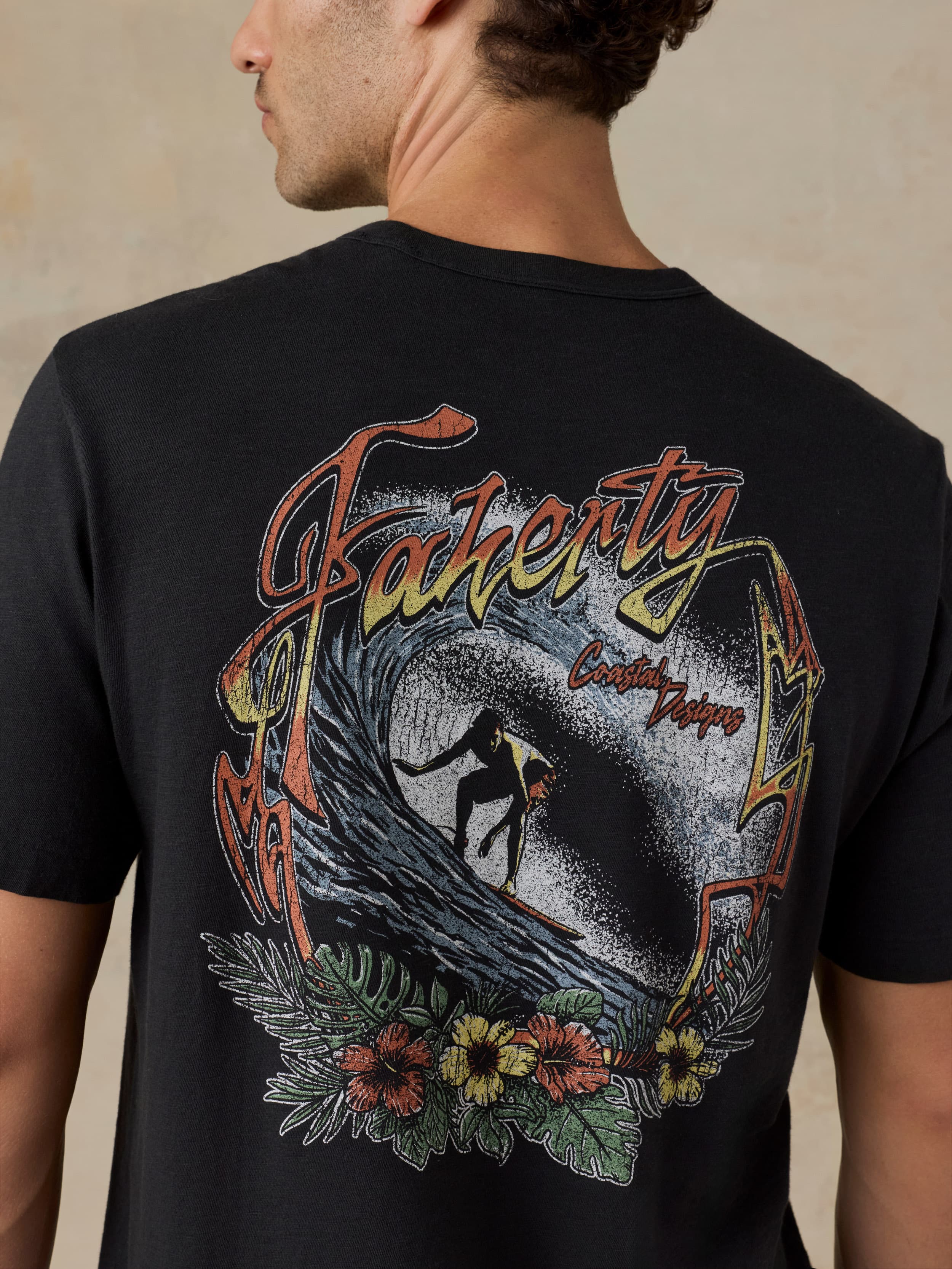 Man wearing a black t-shirt with a colorful graphic design on the back, featuring a surfer and nature elements.