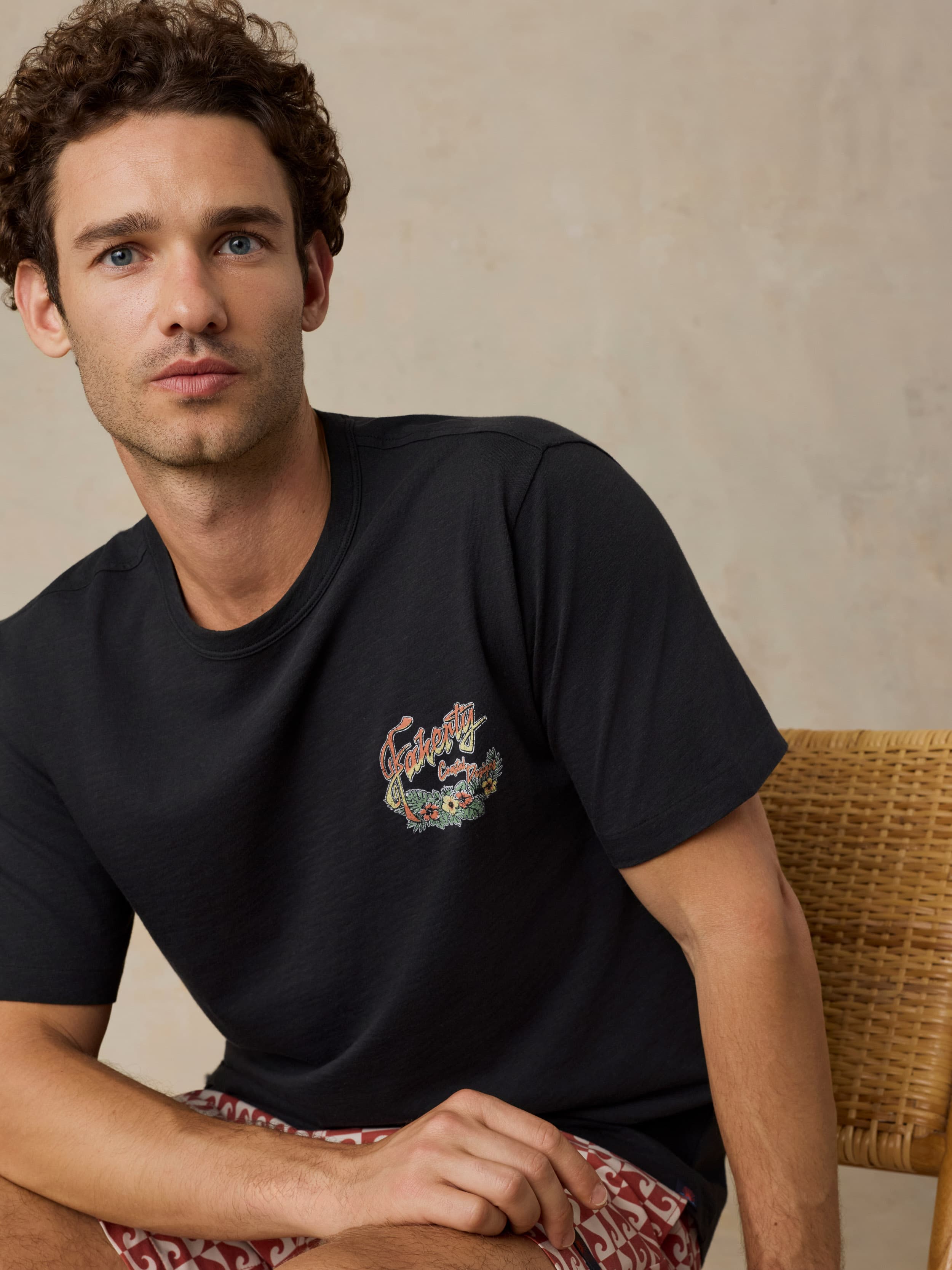 Man wearing a black t-shirt with a colorful logo, sitting against a beige background.