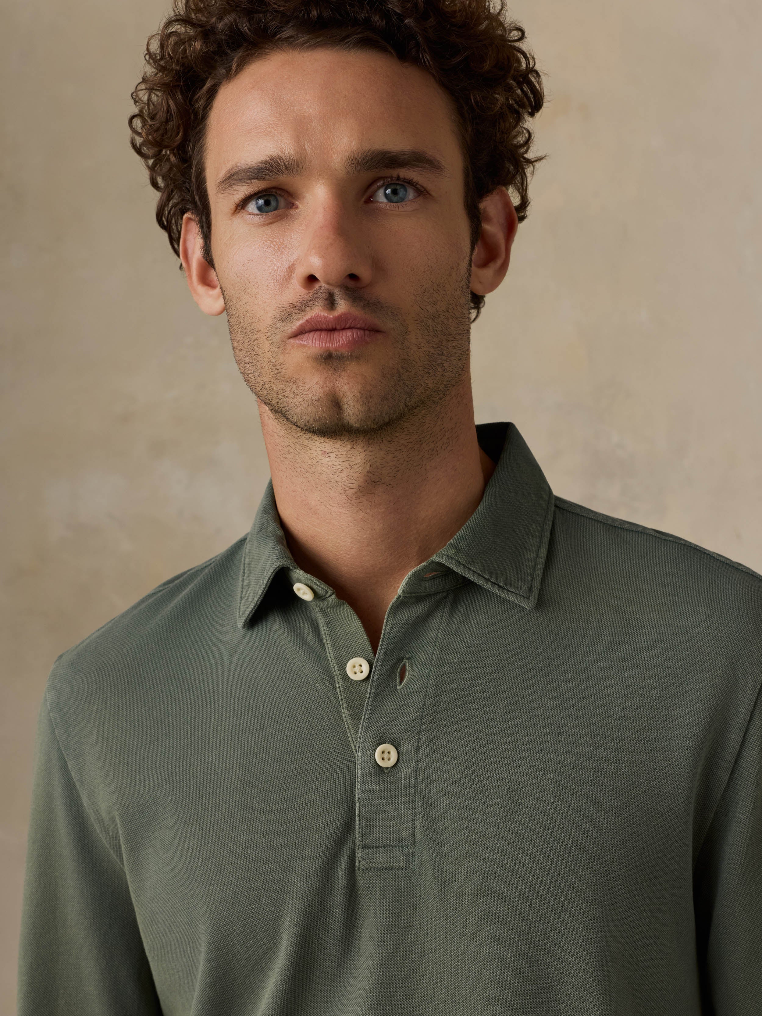 Man wearing a green long-sleeve polo shirt against a beige background