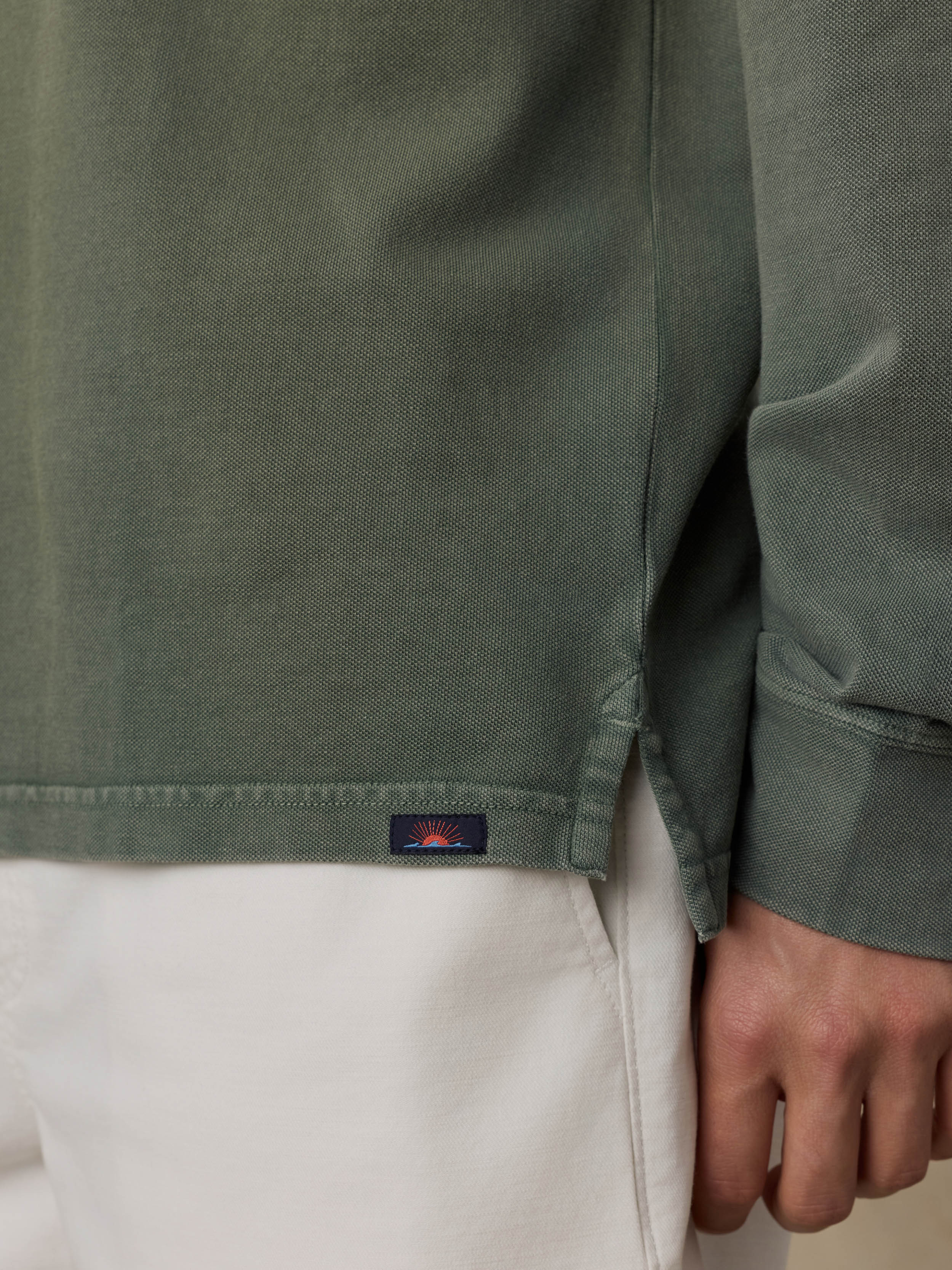 Close-up of a green long-sleeve polo with a Faherty brand logo on a beige background