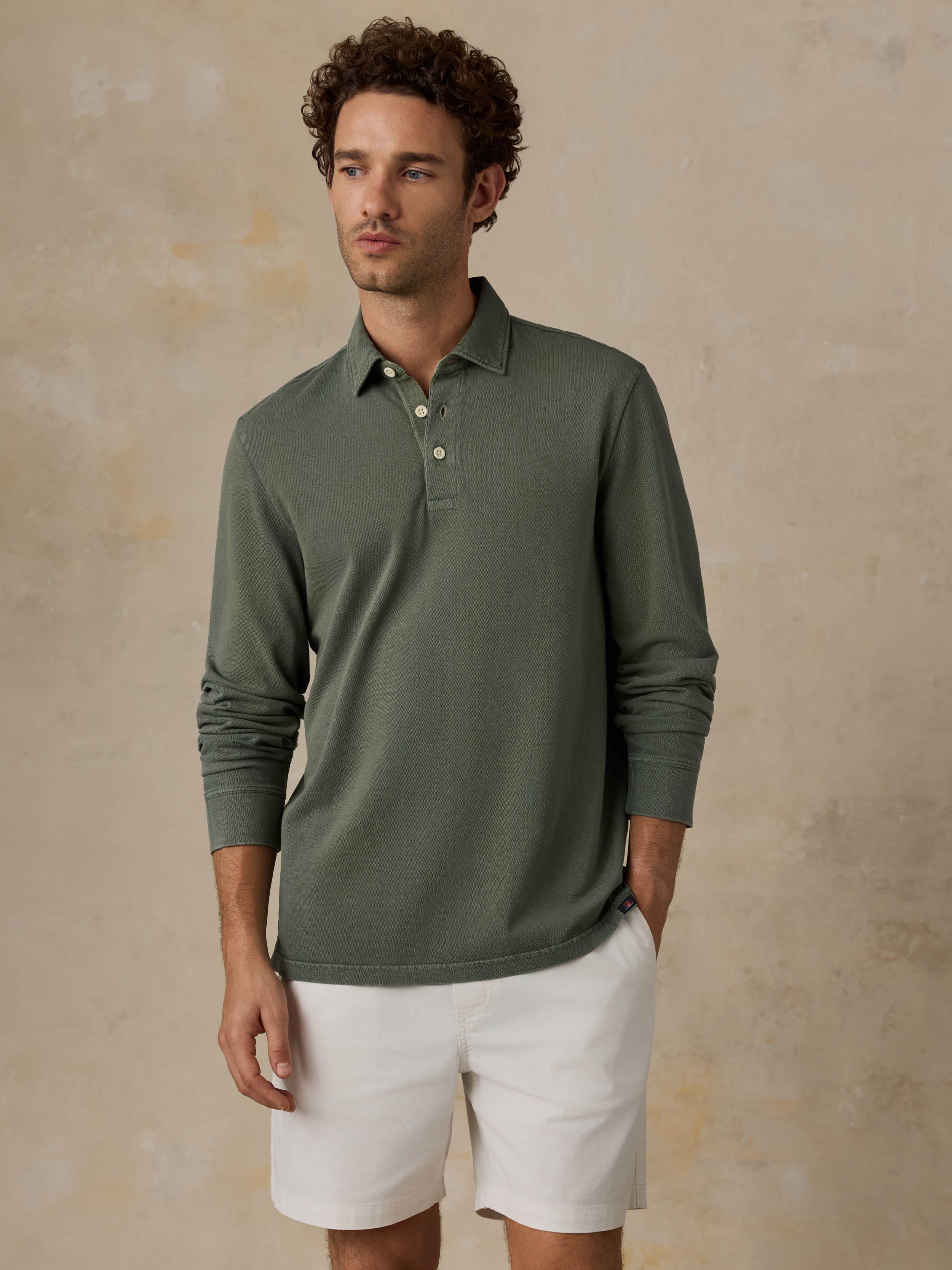 Man wearing a green long-sleeve polo shirt and white shorts against a beige background