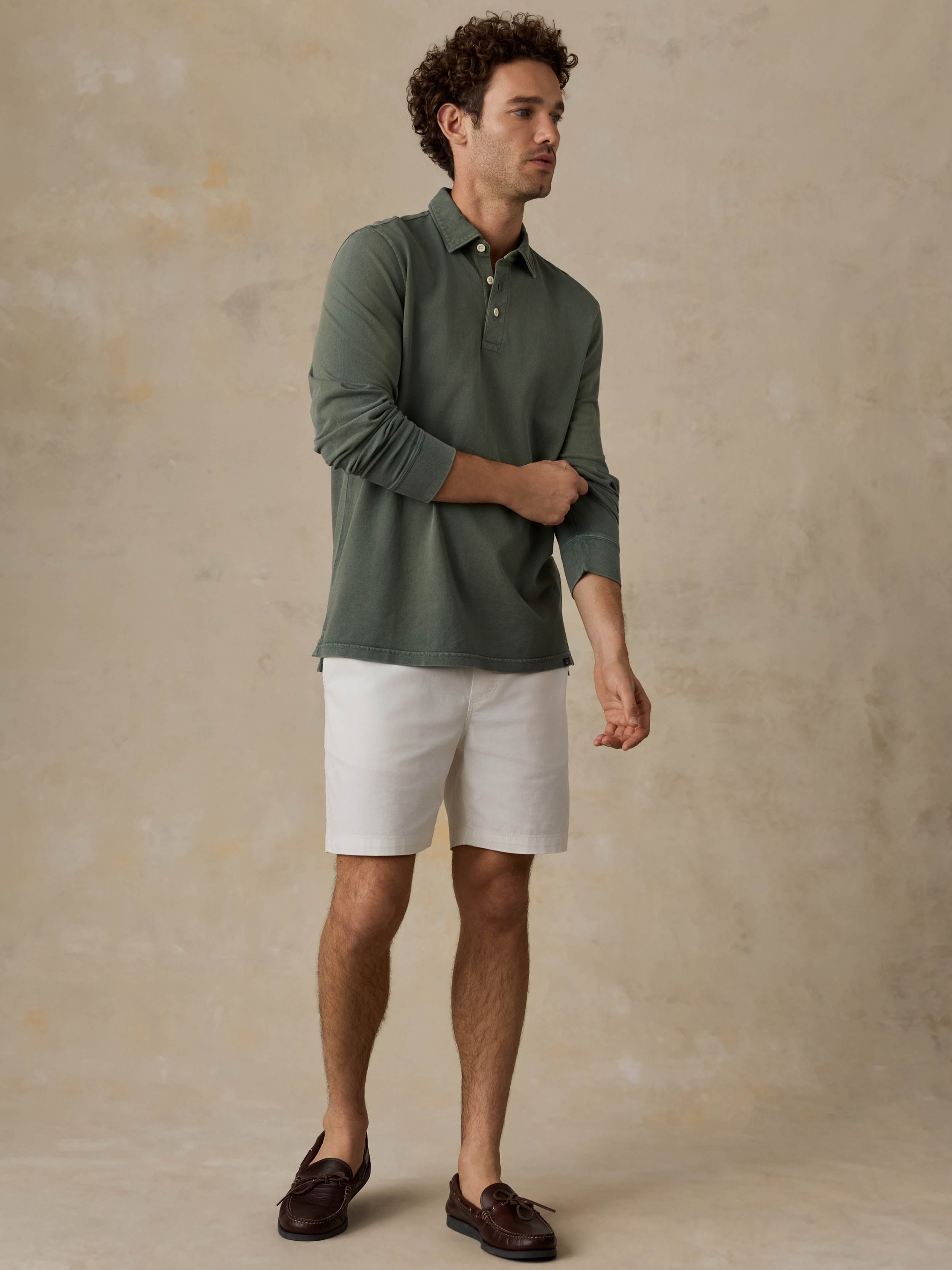 Man wearing a green long-sleeve shirt and white shorts against a beige background