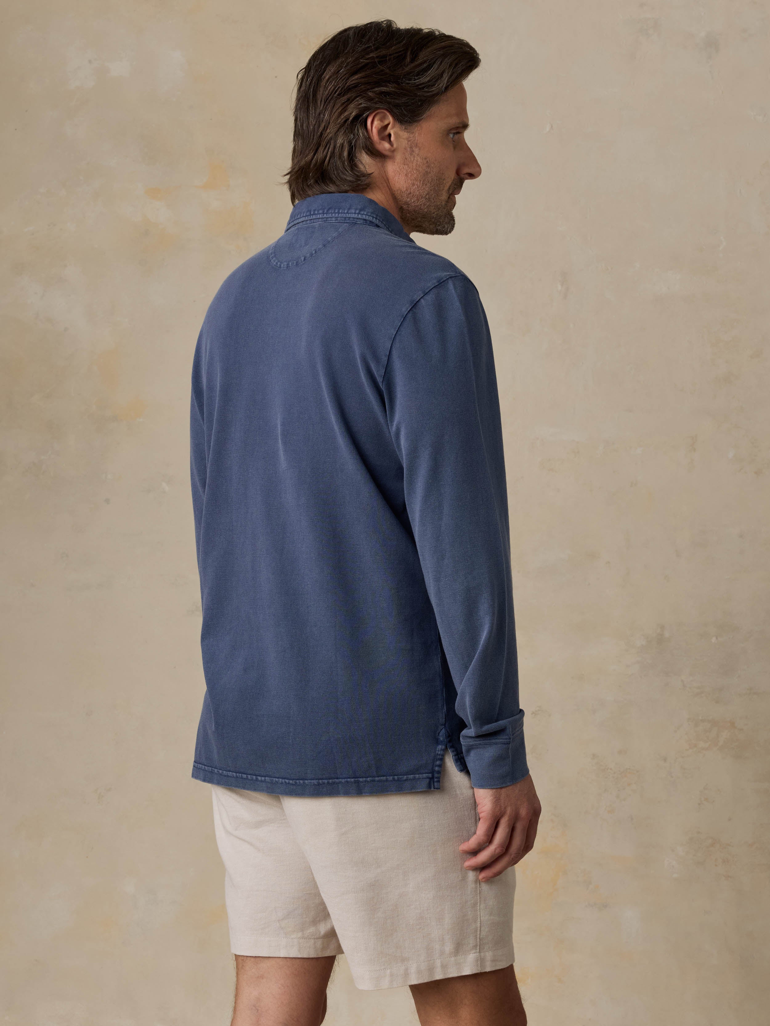 Man wearing a blue long-sleeve polo shirt and beige shorts against a beige background