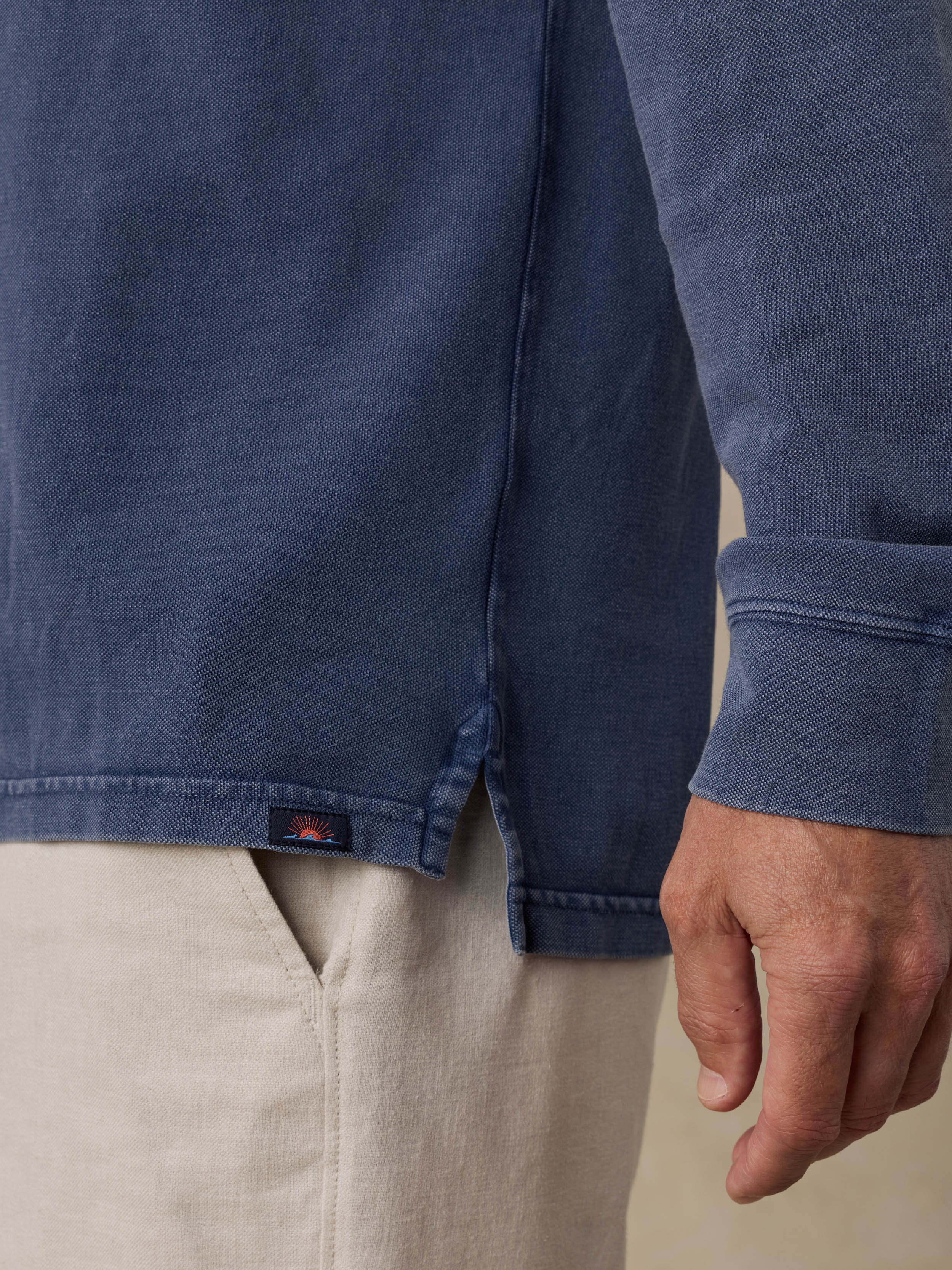 Close-up of a man wearing a blue shirt with a Faherty brand logo and beige shorts