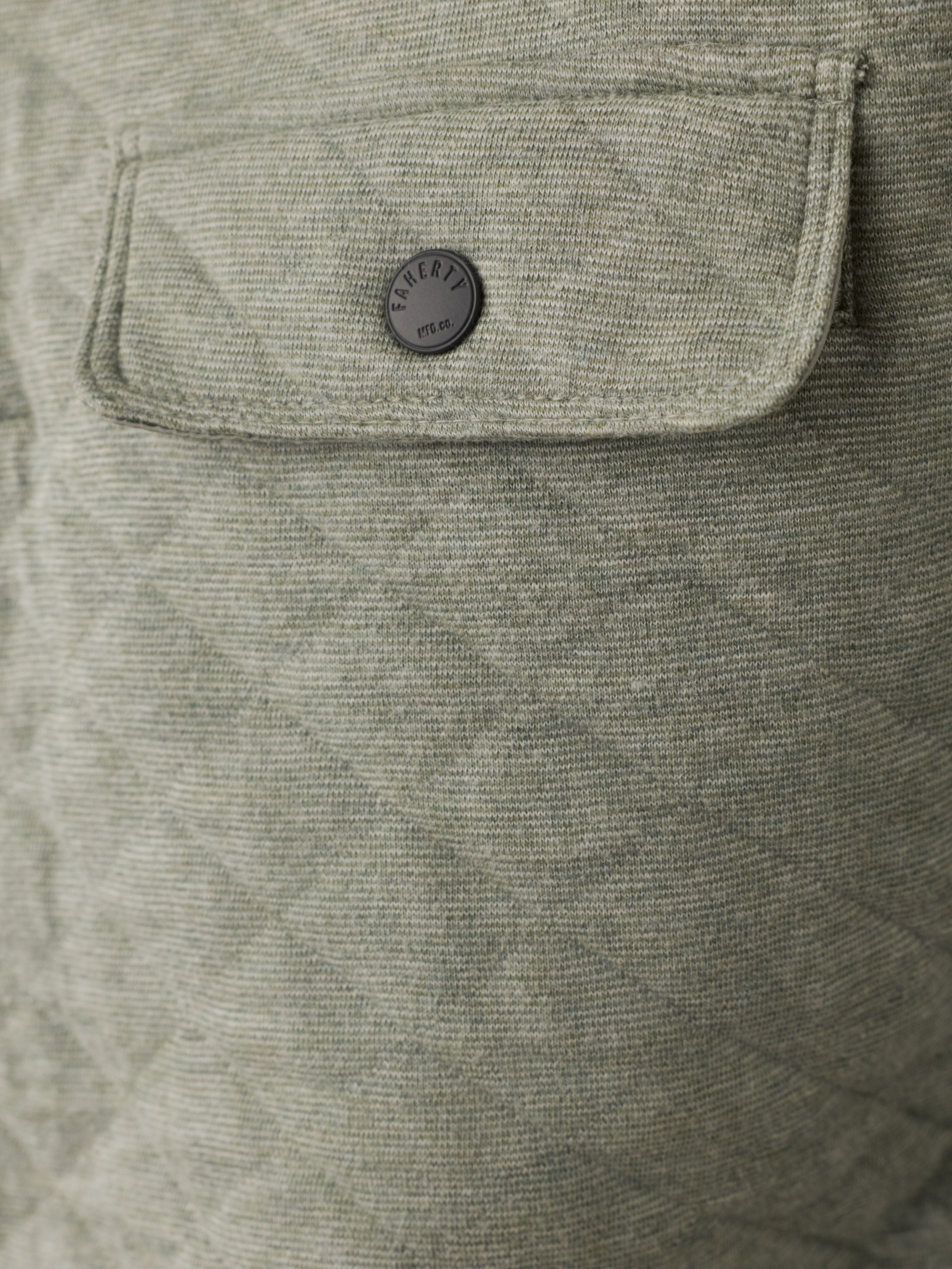 Close-up of a quilted light green fabric jacket with a flap pocket and a round dark gray button featuring the Faherty brand logo.