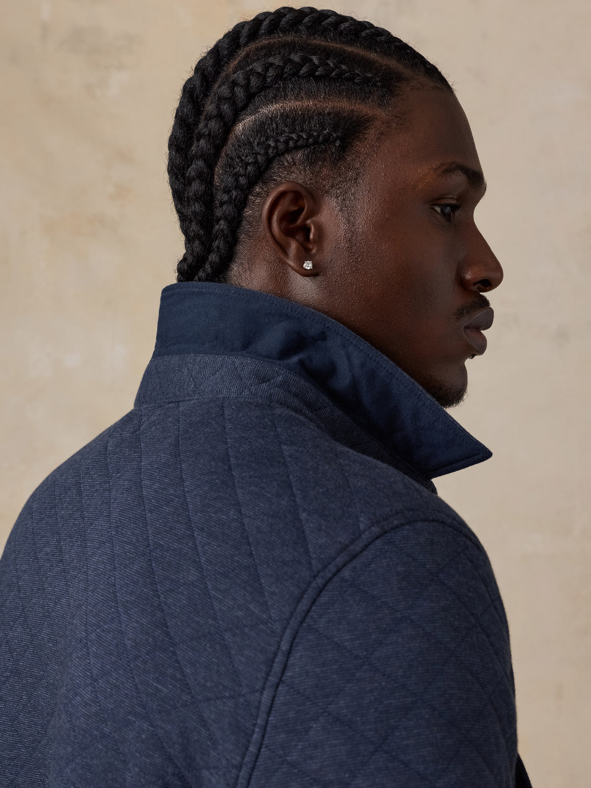 Man wearing a navy quilted jacket against a beige background, image 7 of 7