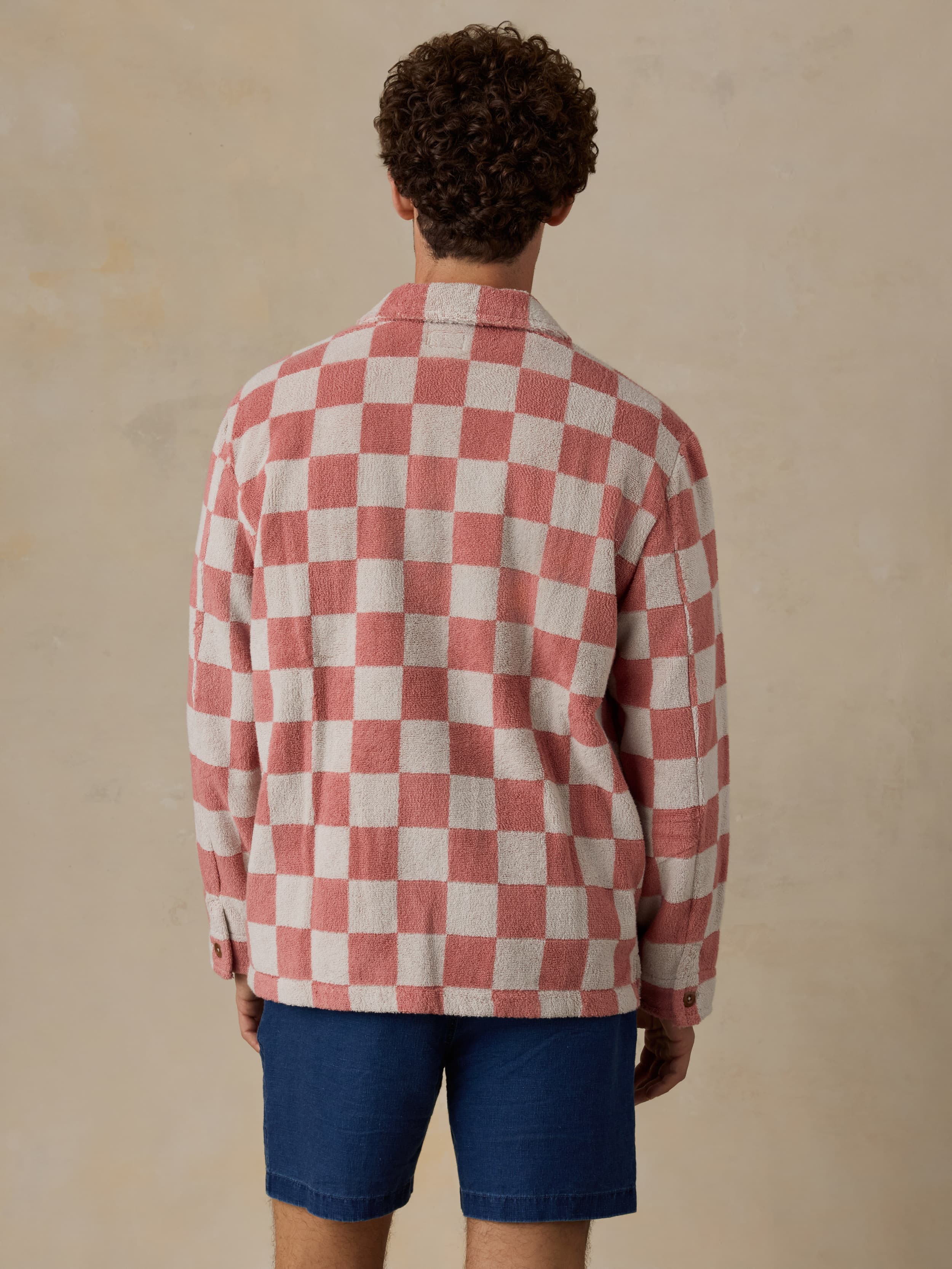 Man wearing a red and white checkered terry jacket with blue shorts on a beige background