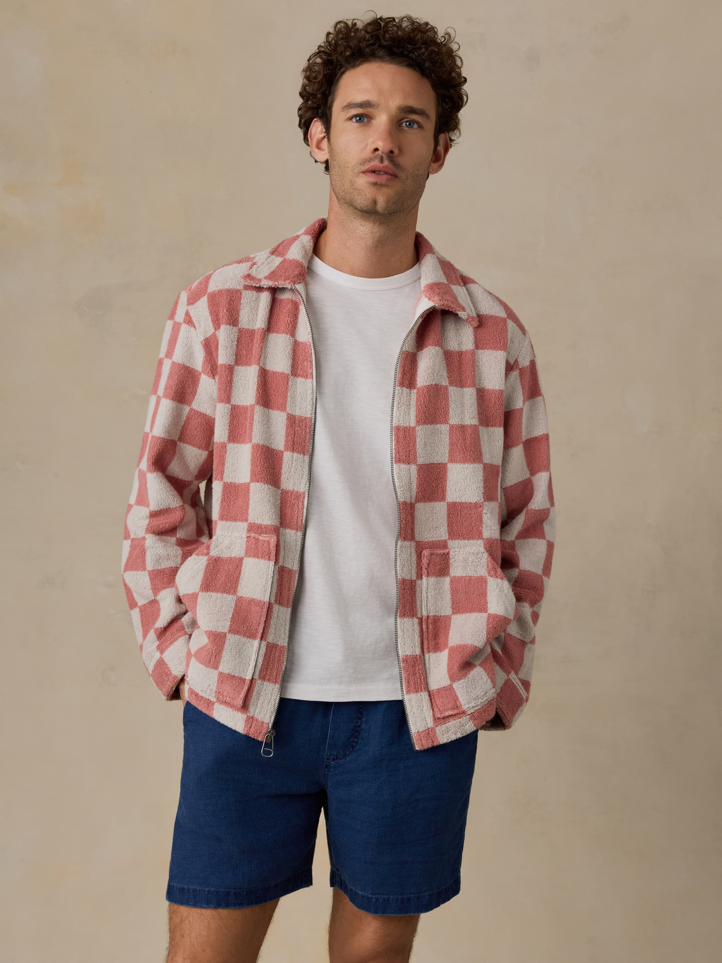 Man wearing a red and white checkered shirt over a white t-shirt and blue shorts on a beige background