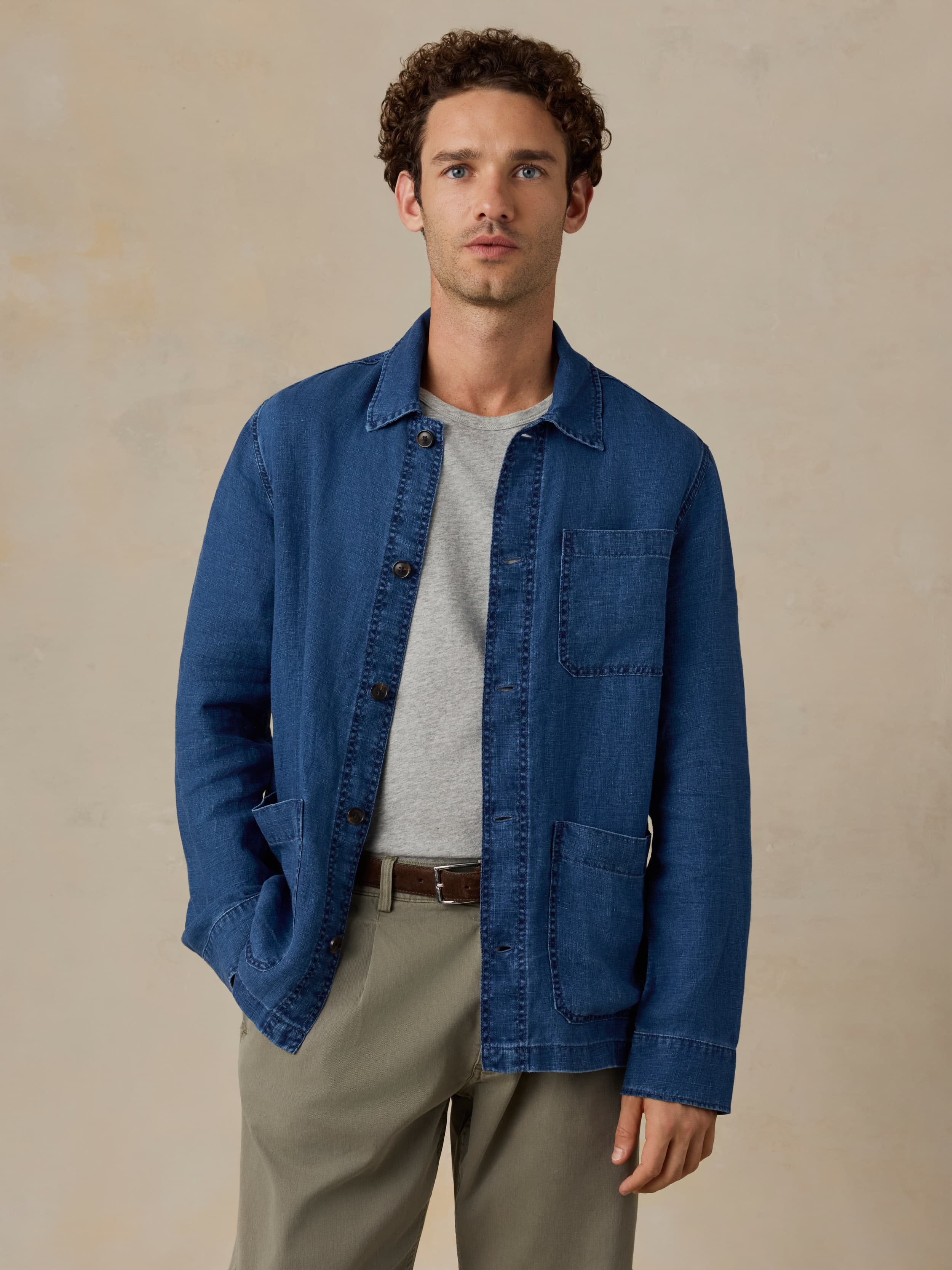 Man wearing a blue denim jacket over a gray shirt on a beige background