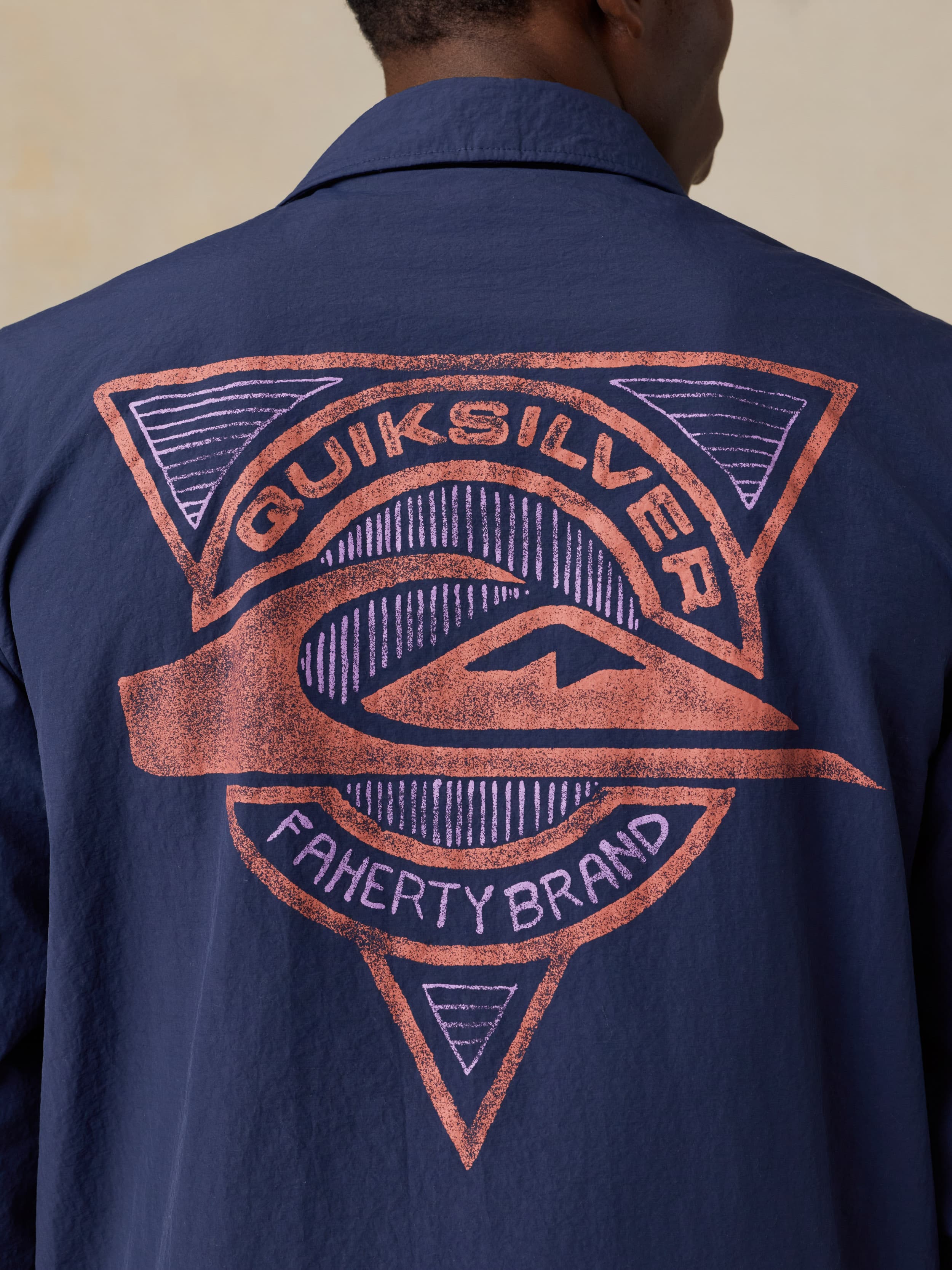 Man wearing a blue jacket with a Quiksilver x Faherty brand logo against a beige background