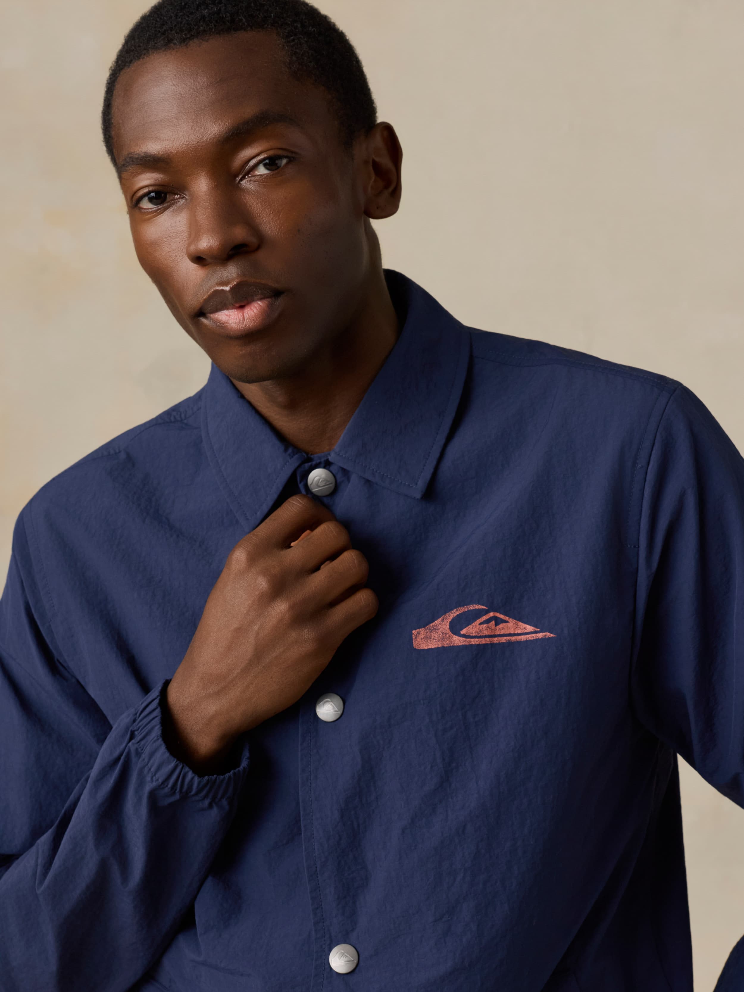 Man wearing a blue jacket with a Quiksilver x Faherty brand logo against a beige background