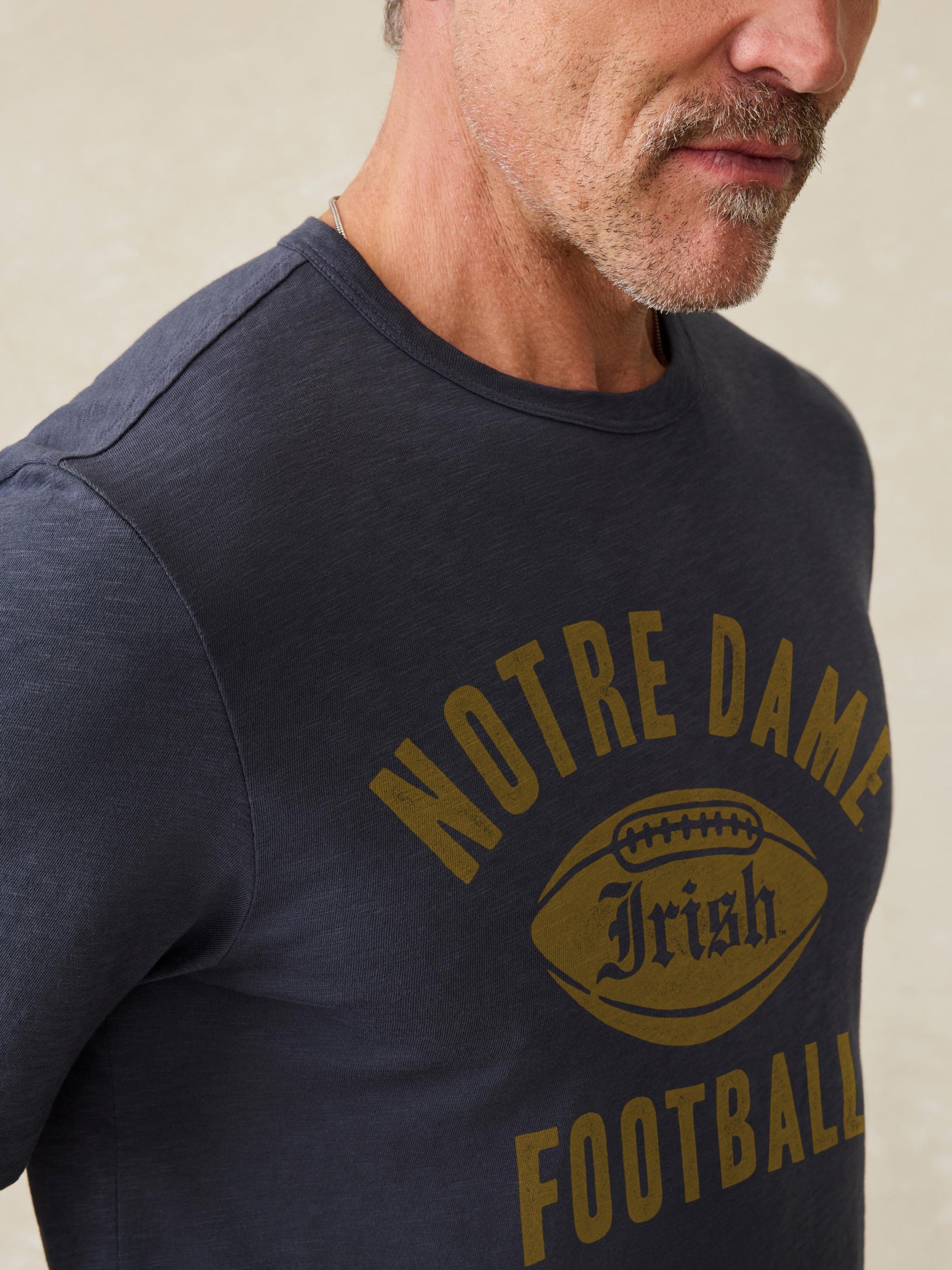 Man wearing a navy short sleeve t-shirt with Notre Dame graphic at the center front against a beige background