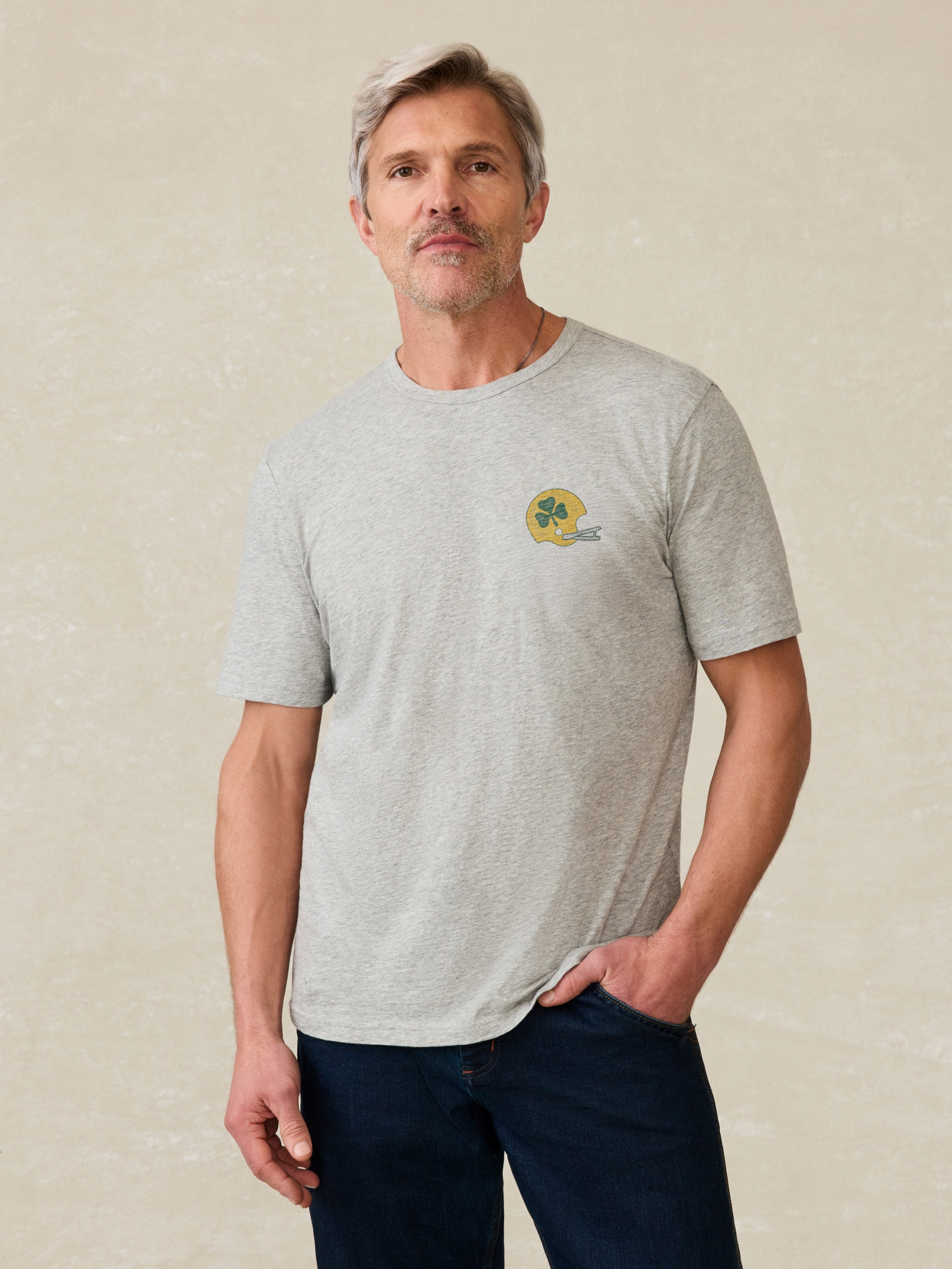 Man wearing a gray t-shirt with 'Notre Dame Football' graphic chest against a beige background