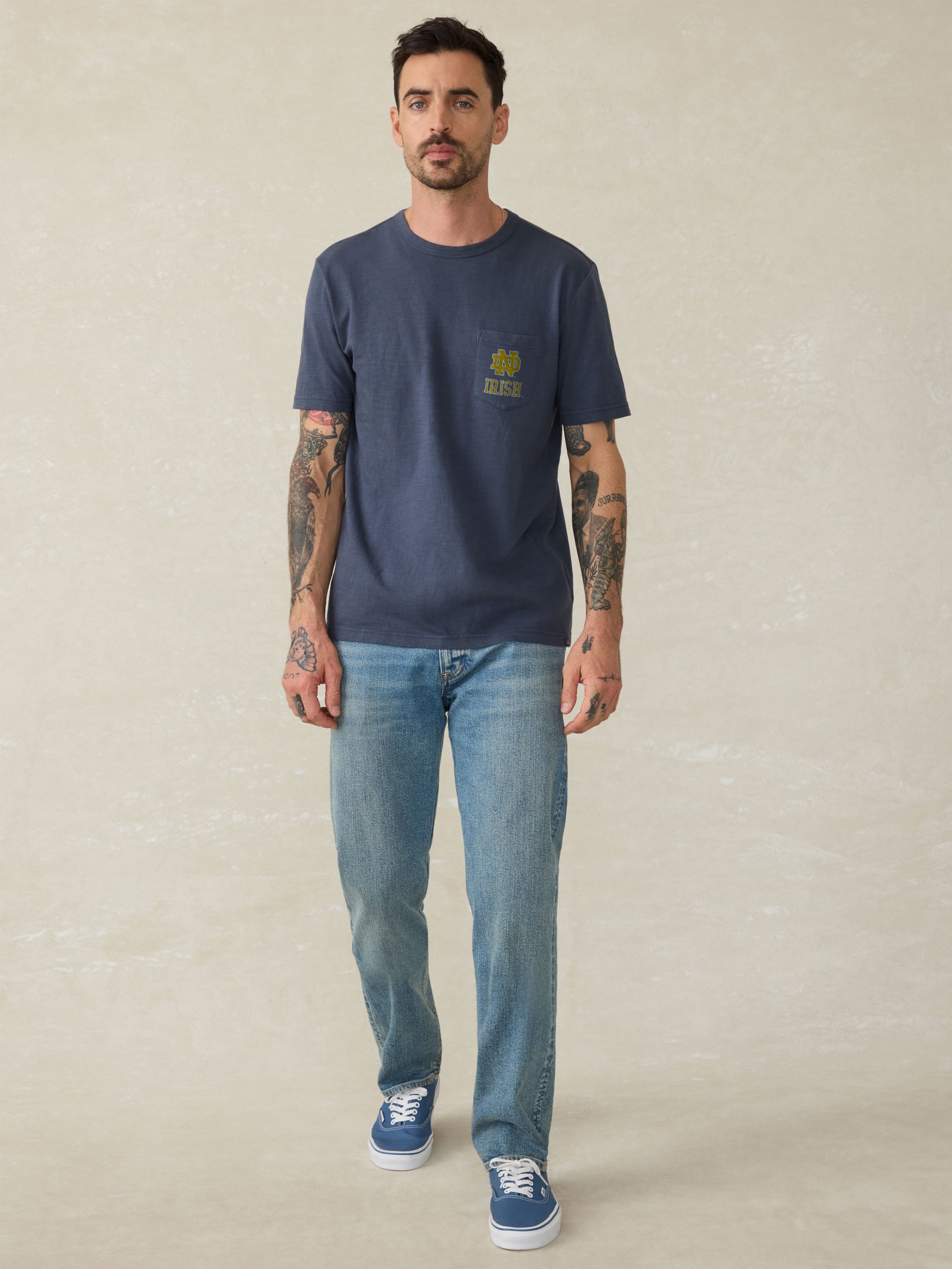 Man wearing a navy blue t-shirt with a Notre Dame logo on the chest against a beige background