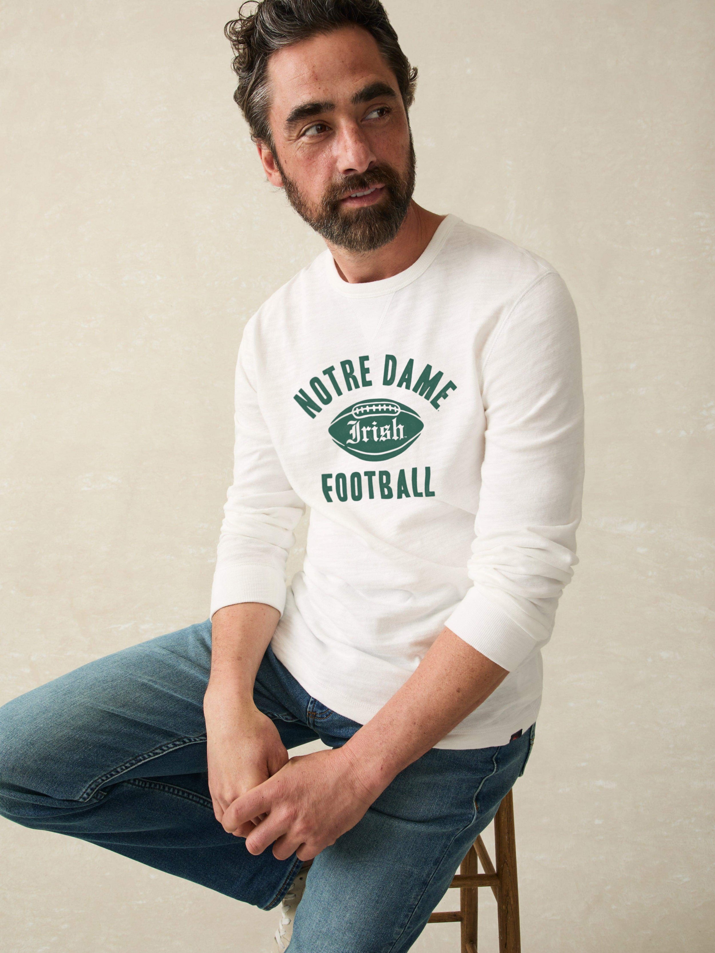 Man wearing a white long-sleeve shirt with 'Notre Dame Football' graphic on a beige background