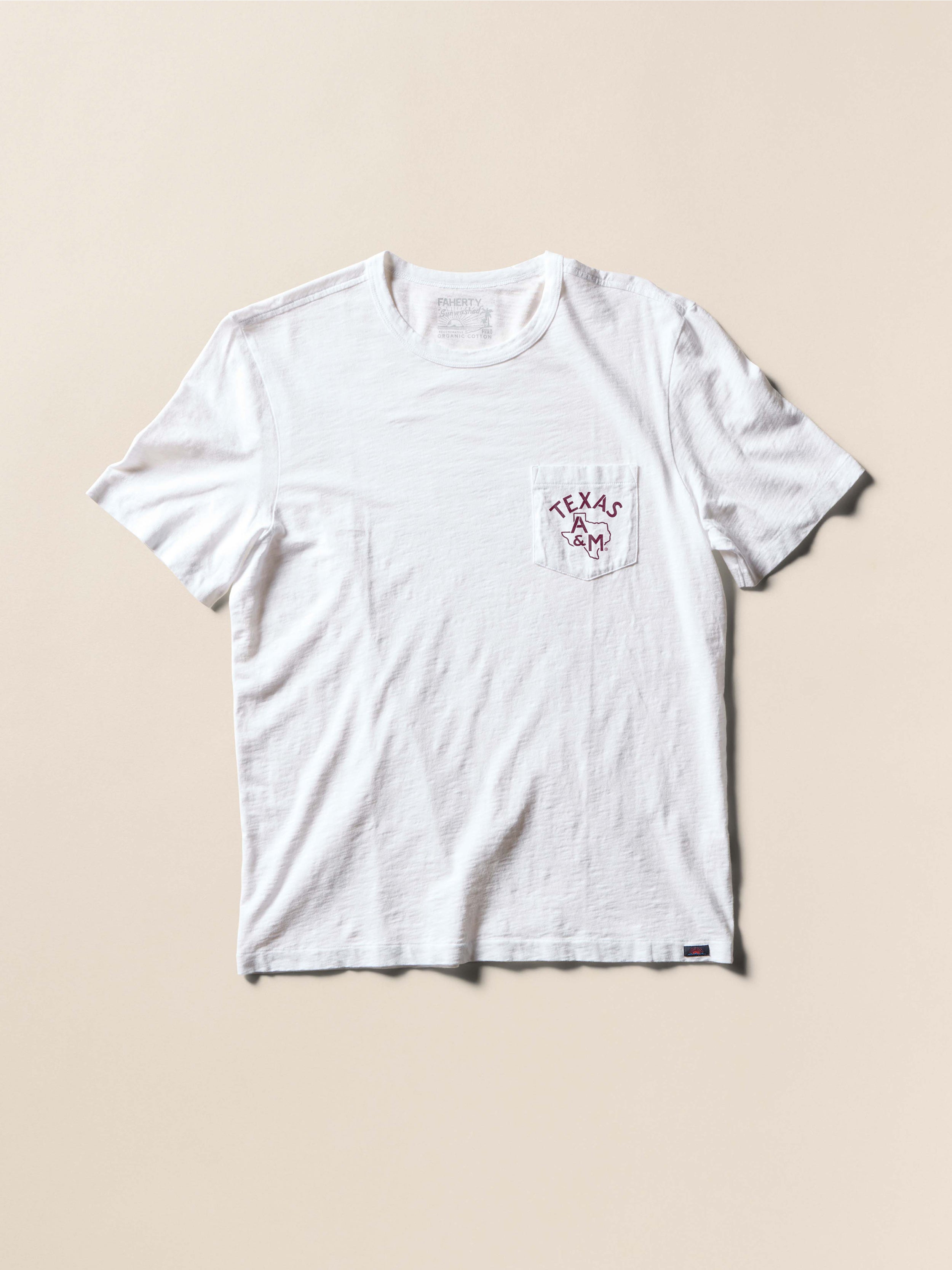 White t-shirt with Texas A&M graphic on front left chest pocket against a beige background