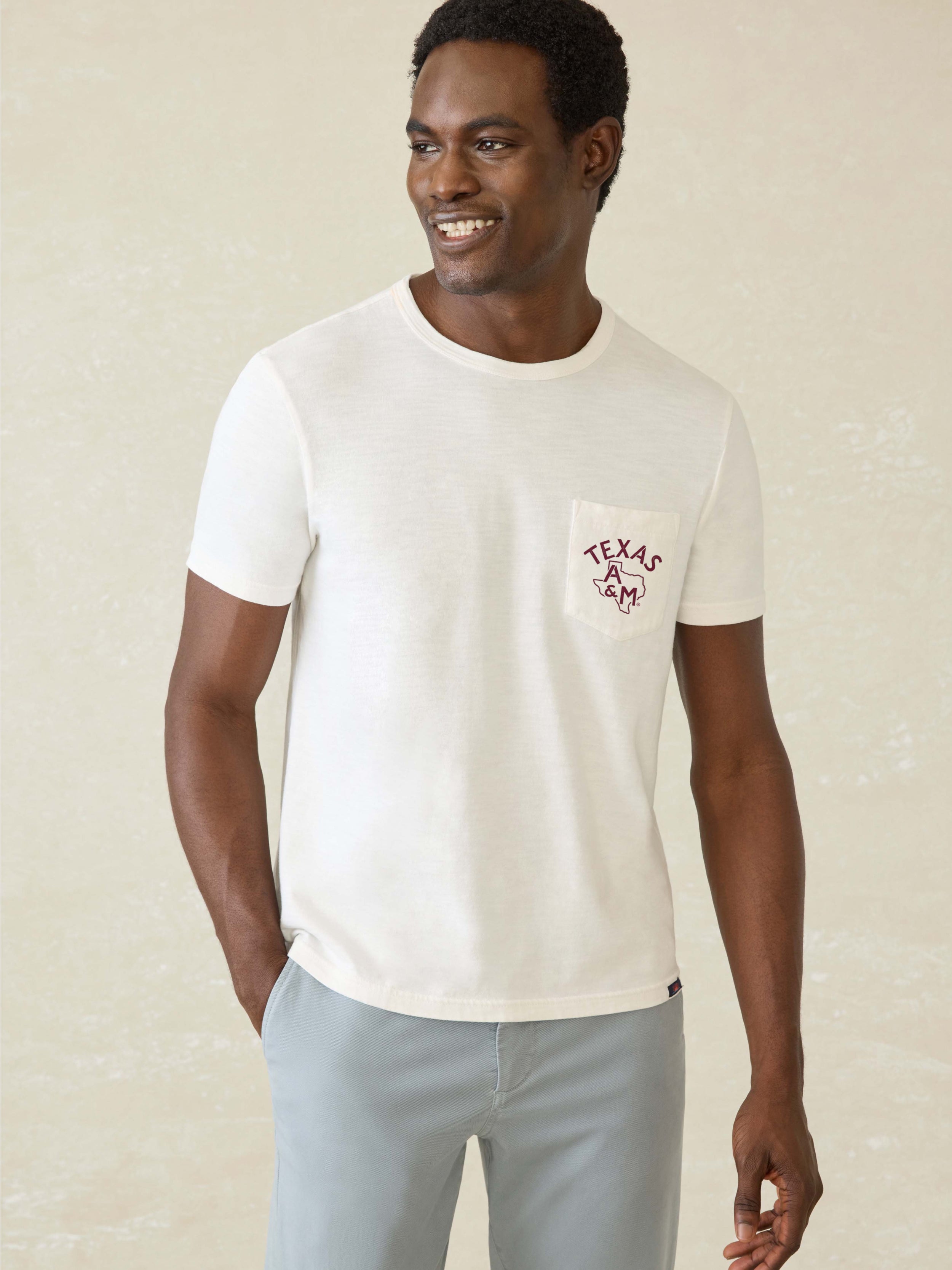 Man wearing a white t-shirt with Texas A&M graphic on front left chest pocket against a beige background