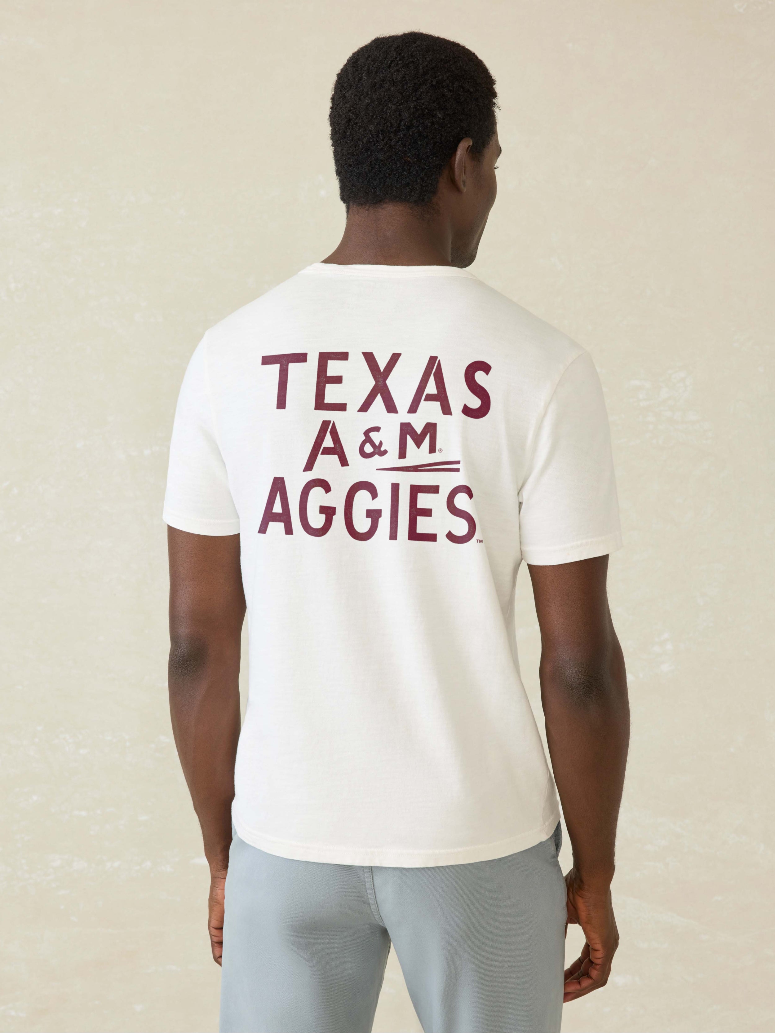 Man wearing a white t-shirt with Texas A&M graphic on front left chest pocket against a beige background