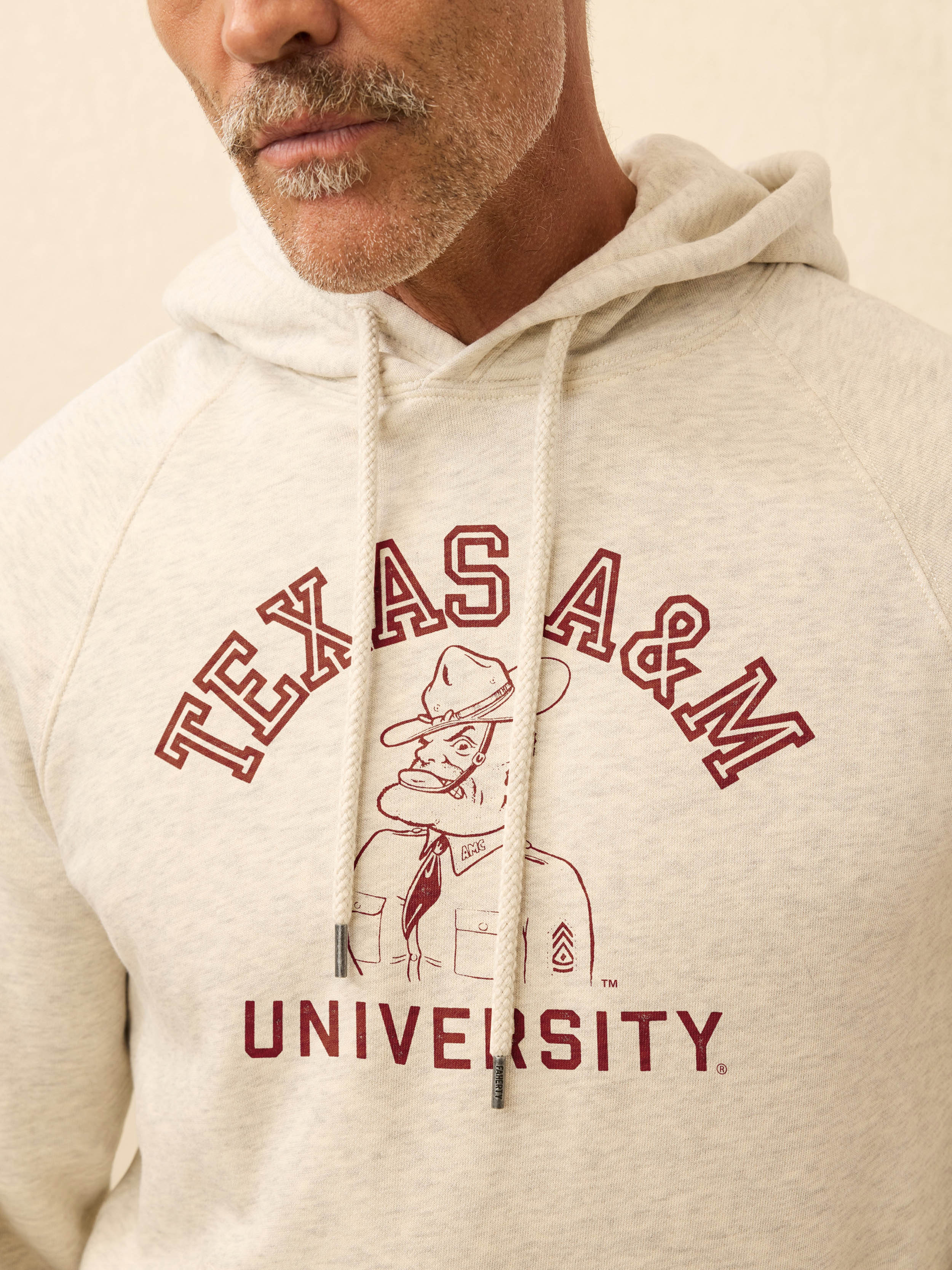 Man wearing an ivory hooded sweatshirt with Texas A&M graphic at the front against a beige background