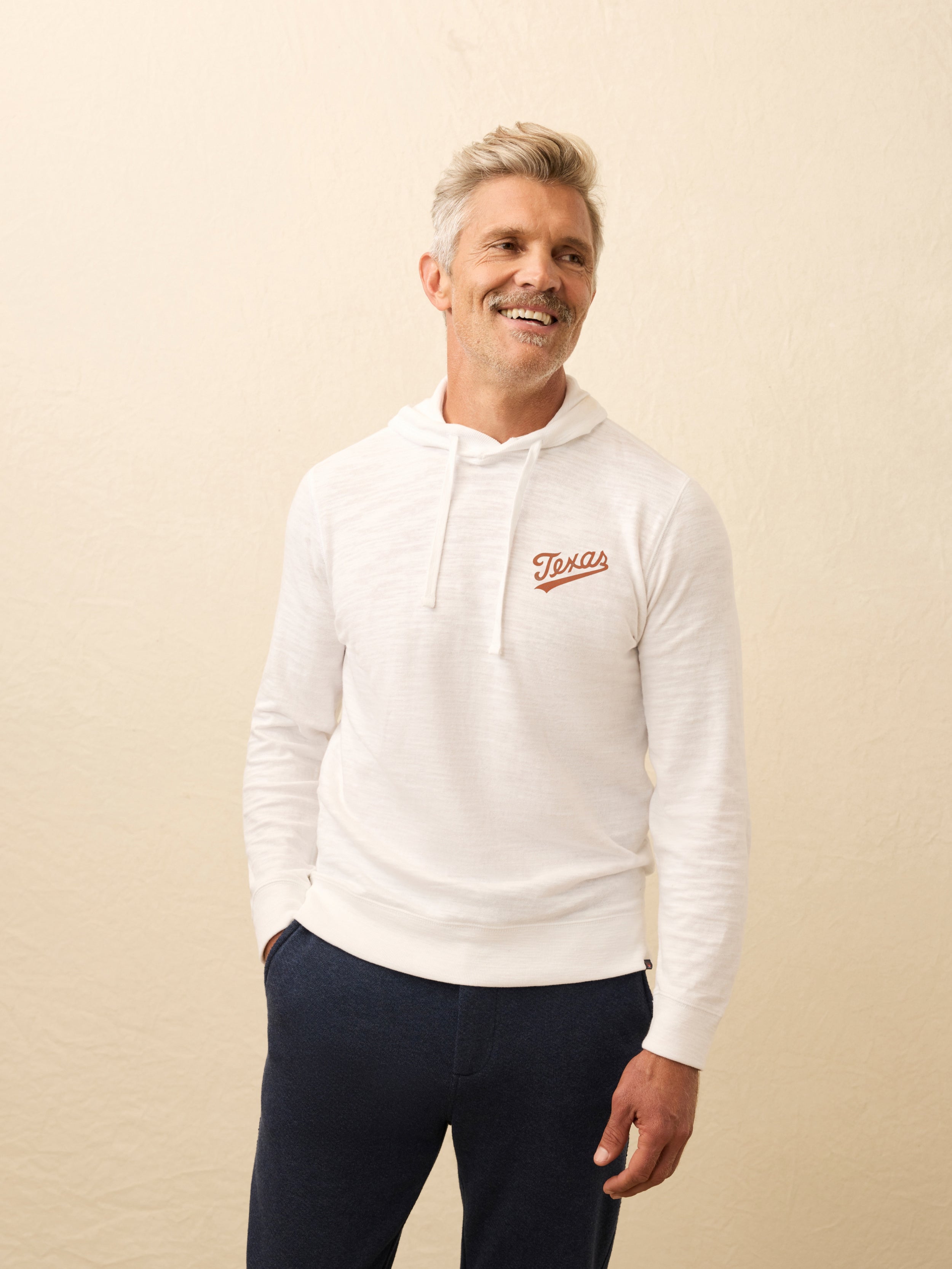 Man wearing a white hoodie with UT Austin graphic on the left chest against a beige background