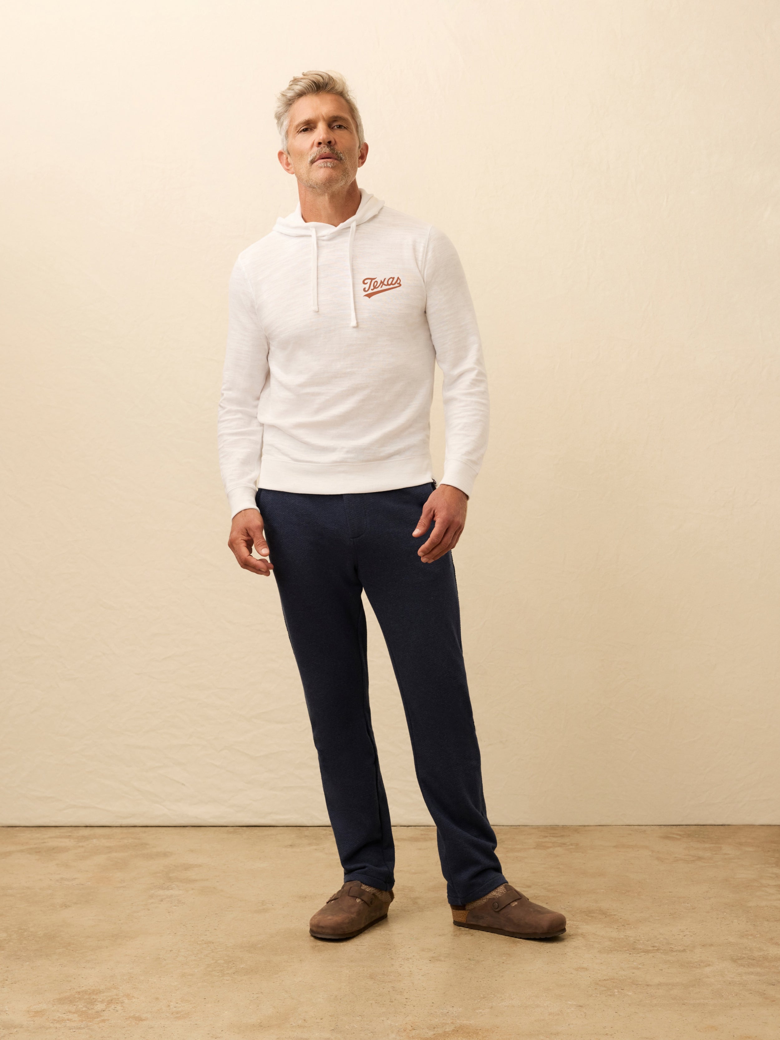 Man wearing a white hoodie with UT Austin graphic on the left chest against a beige background